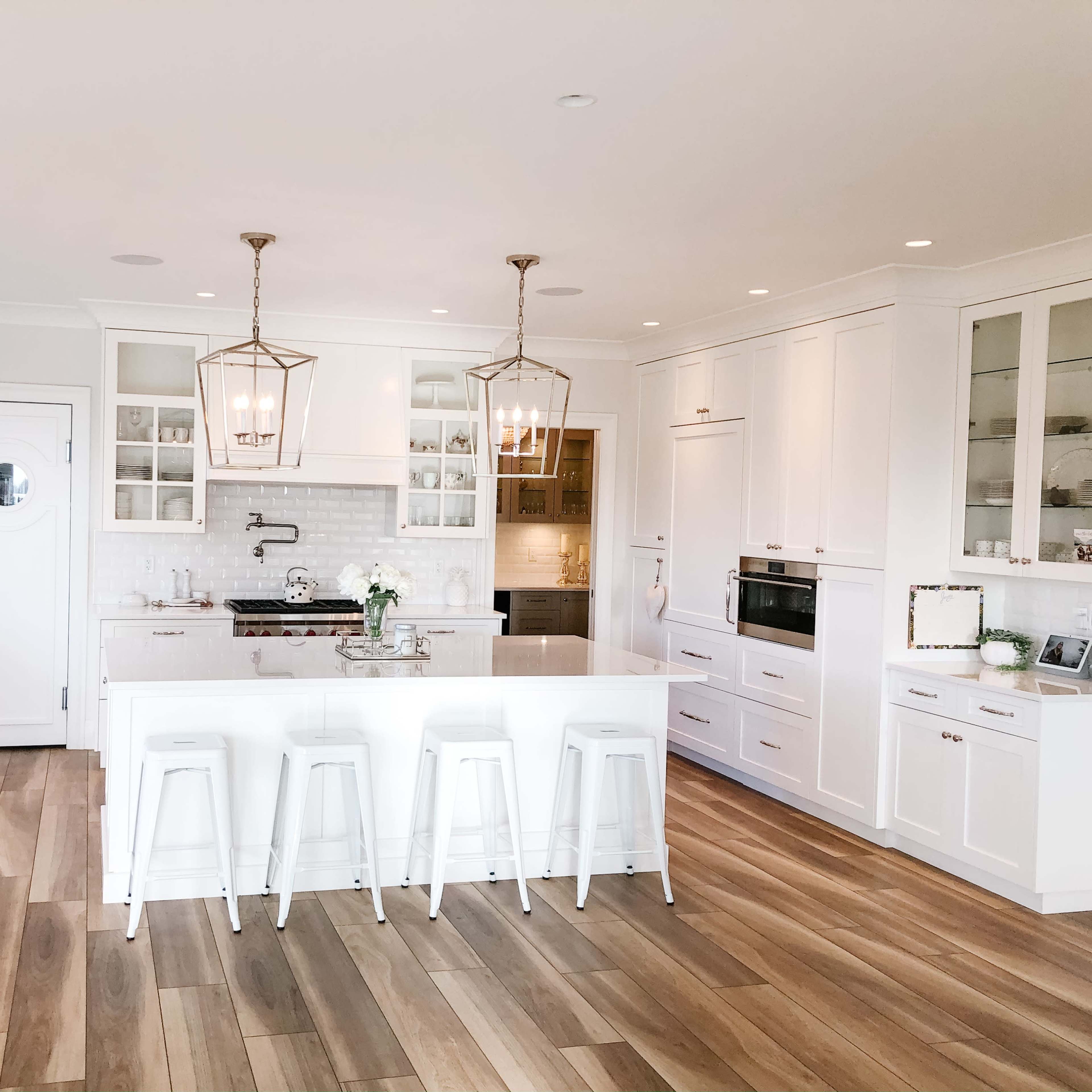 A modern kitchen features white cabinetry, a central island with bar stools, and wooden flooring.