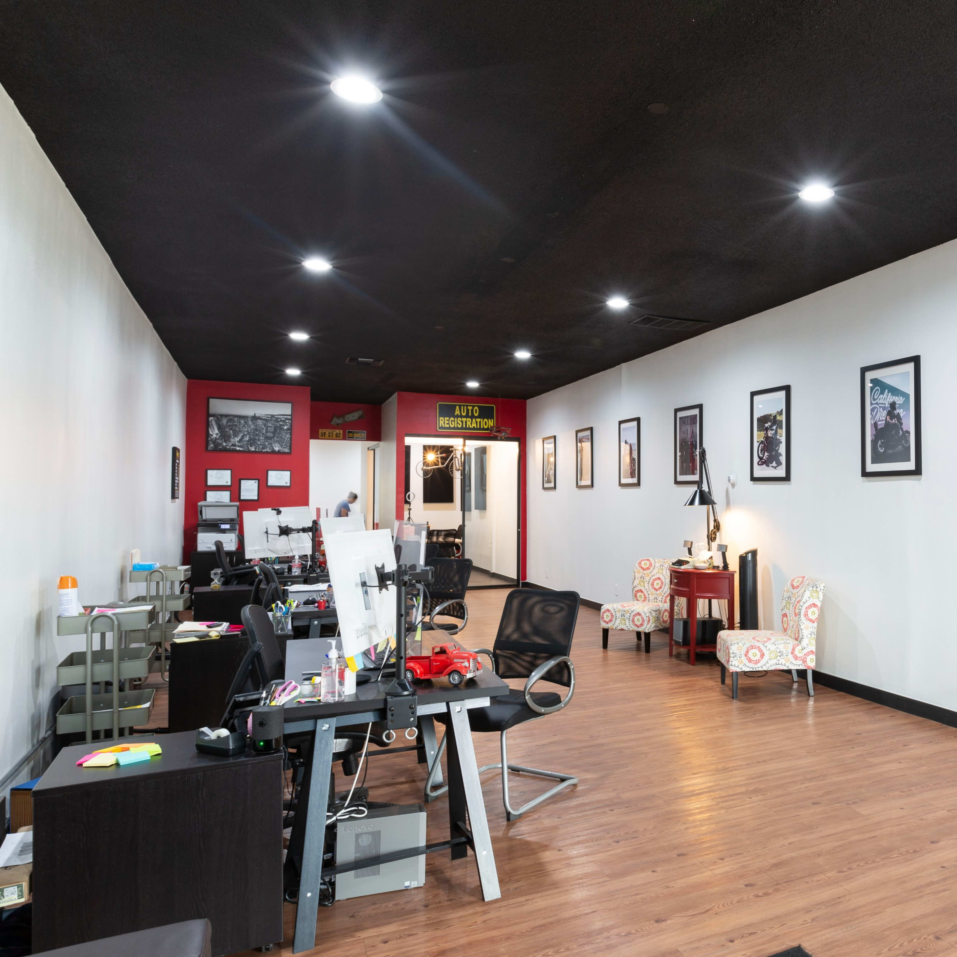 An office space with desks on one side, seating areas with chairs, and framed pictures on the walls.