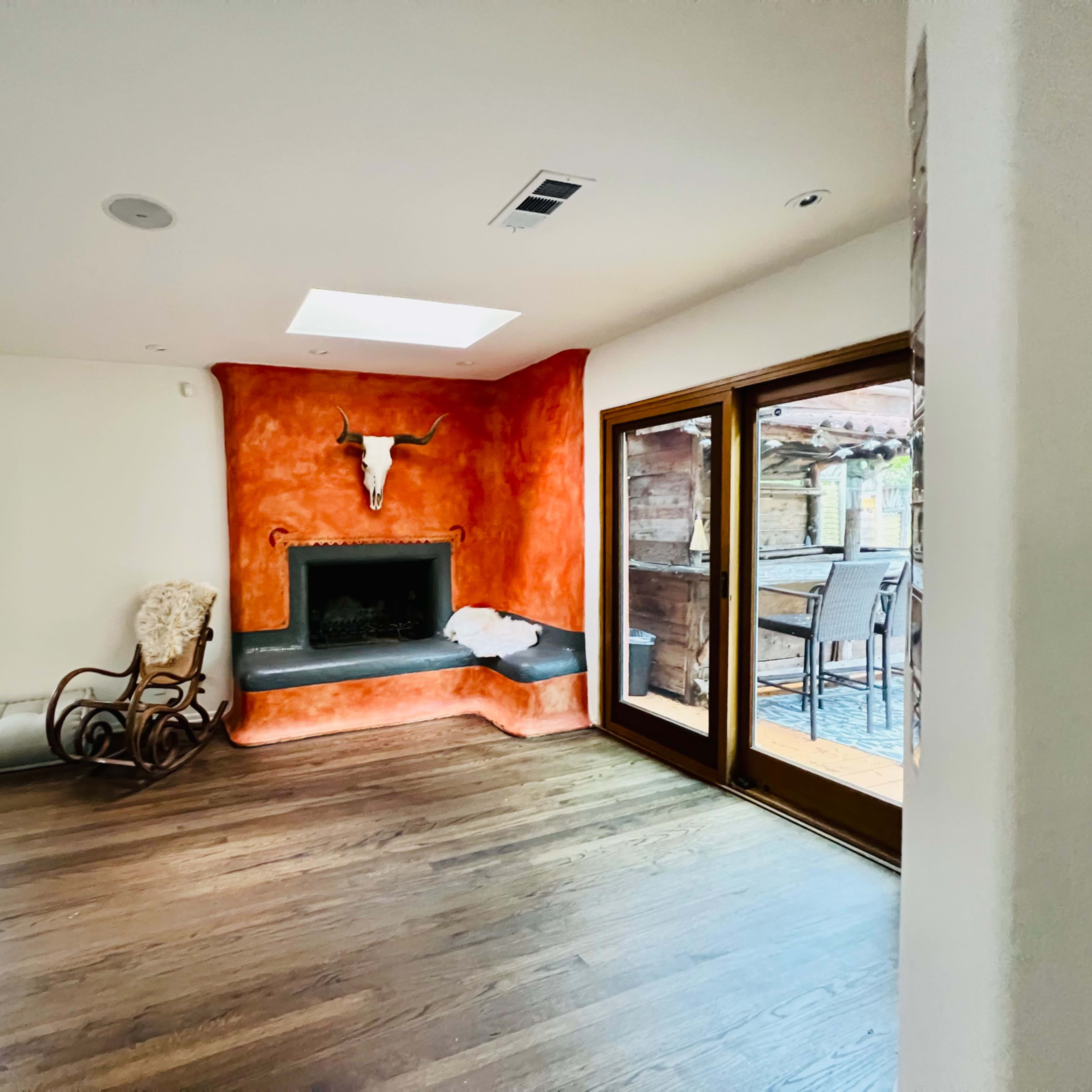 A living room with a large fireplace featuring a bull's head mounted on the orange wall, hardwood floors, and sliding glass doors leading to an outdoor patio area.