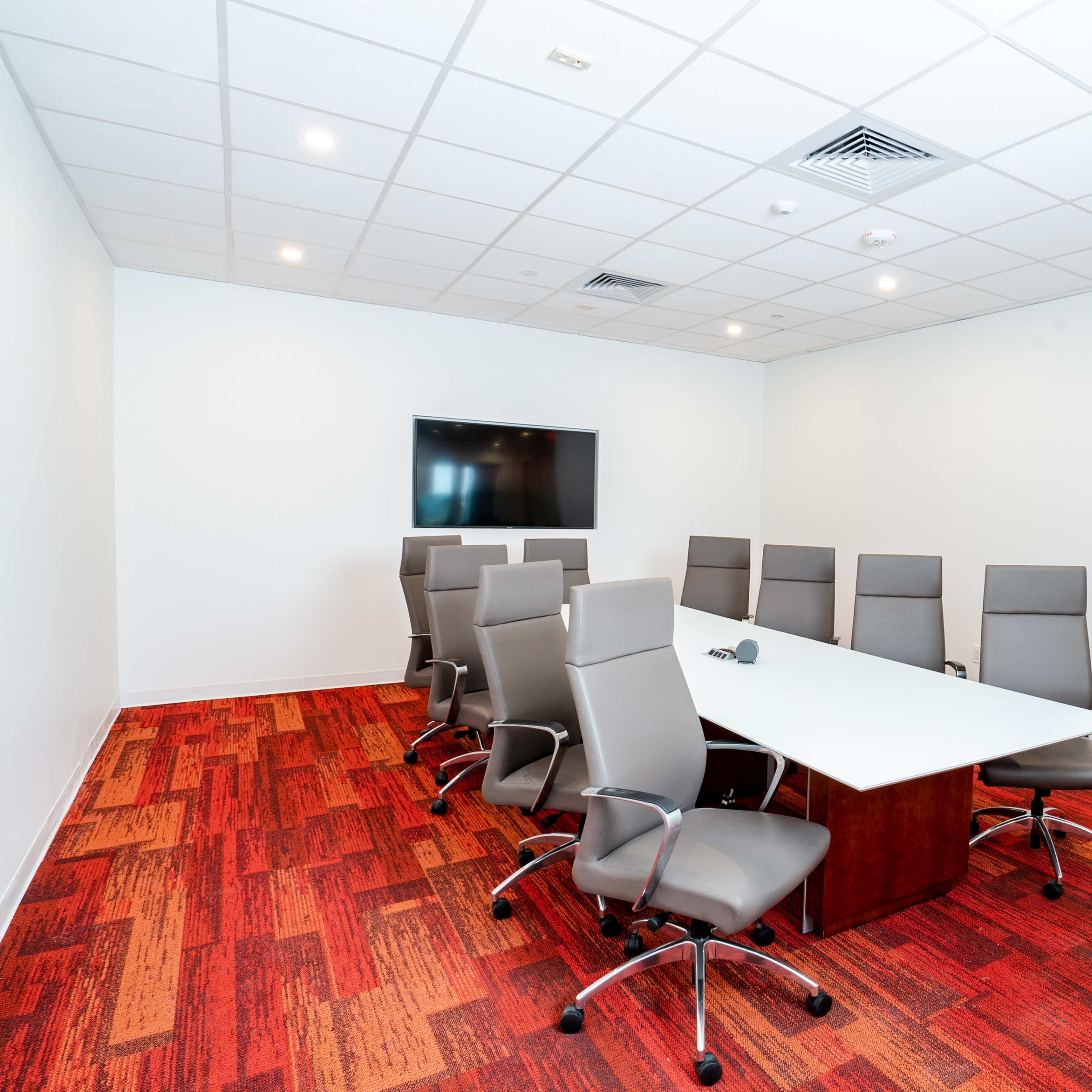 A modern conference room with a rectangular table surrounded by eight ergonomic chairs and a wall-mounted screen.