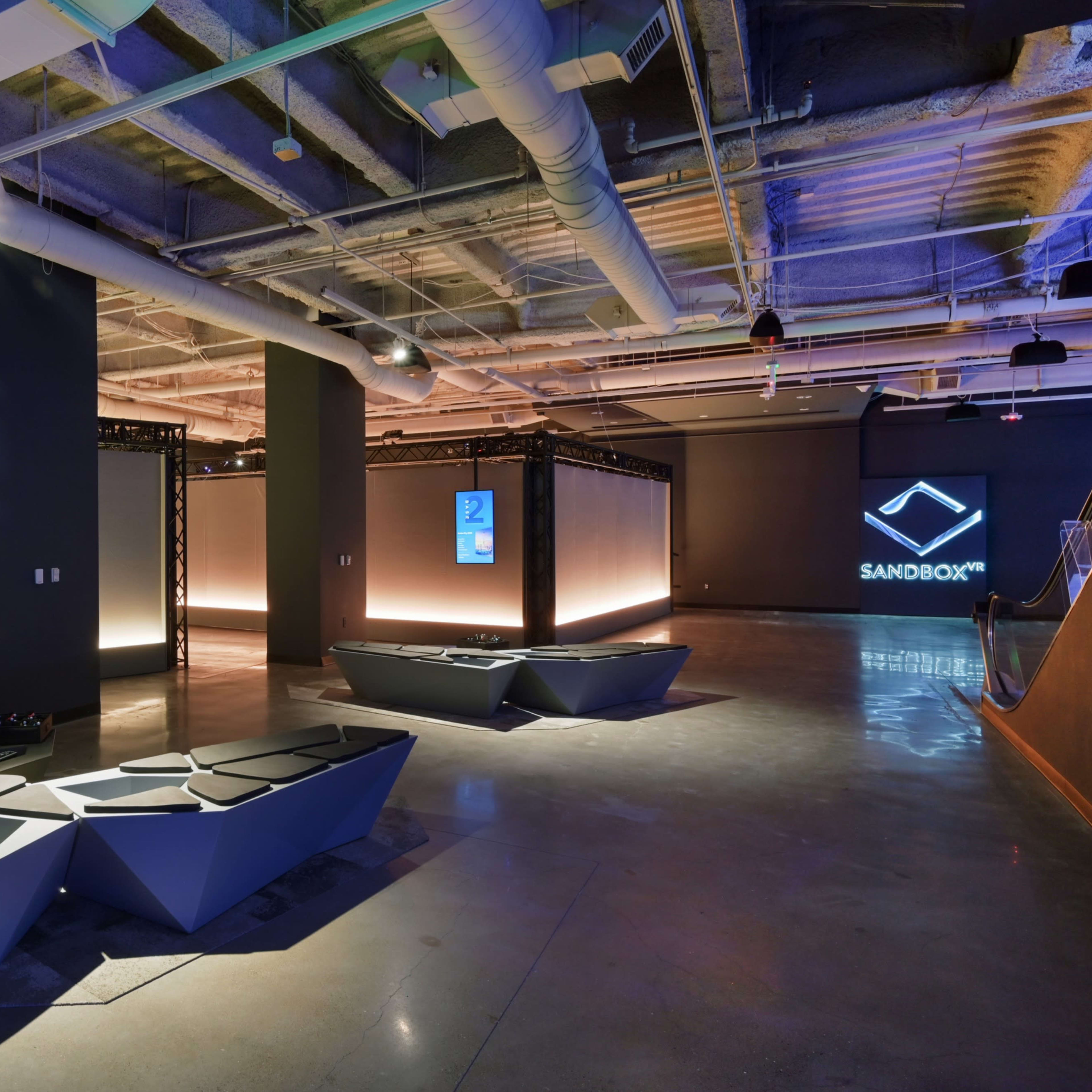 A modern, minimalist lounge area with angular seating and illuminated display panels in a spacious interior.