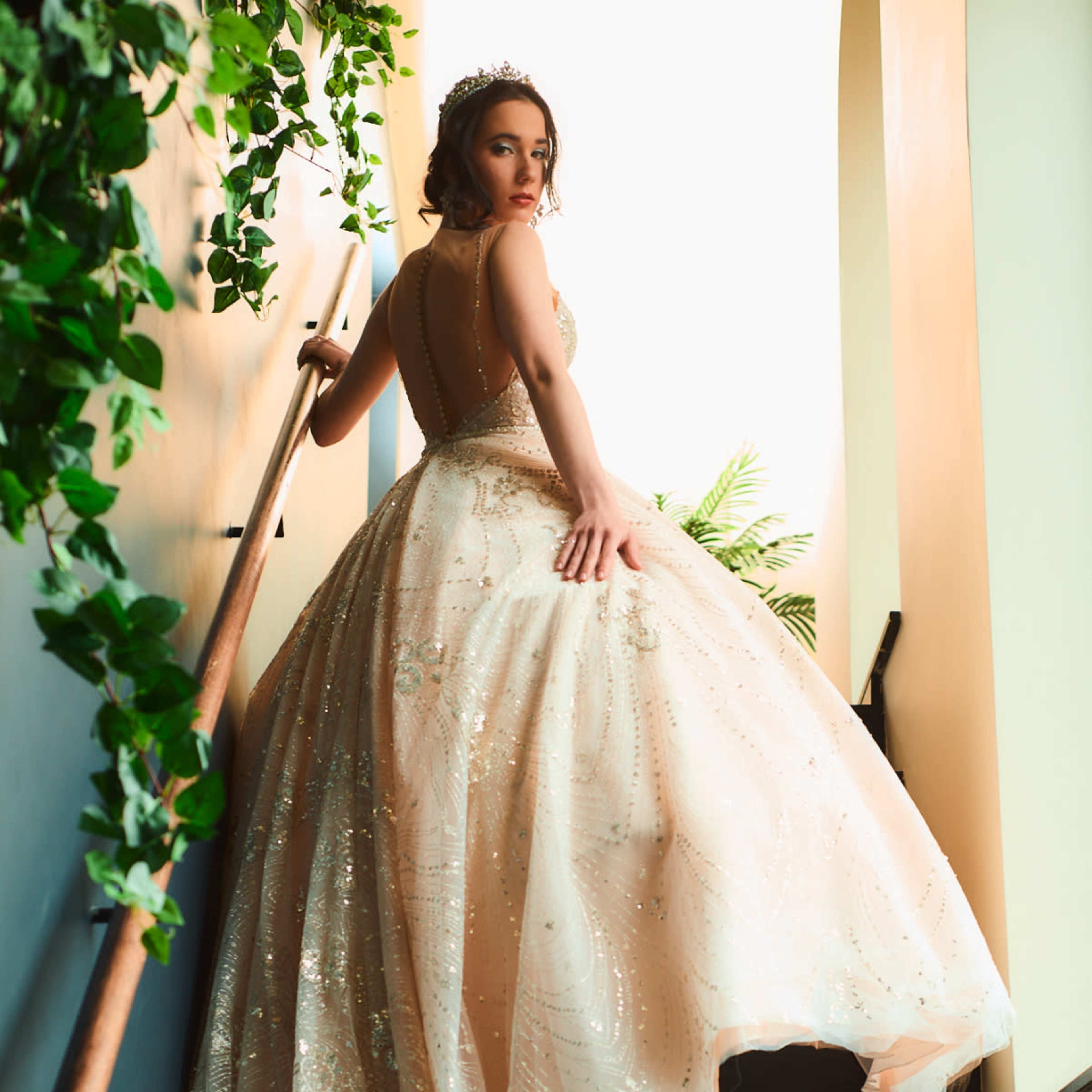 A woman in a beaded gown ascends a staircase adorned with greenery.