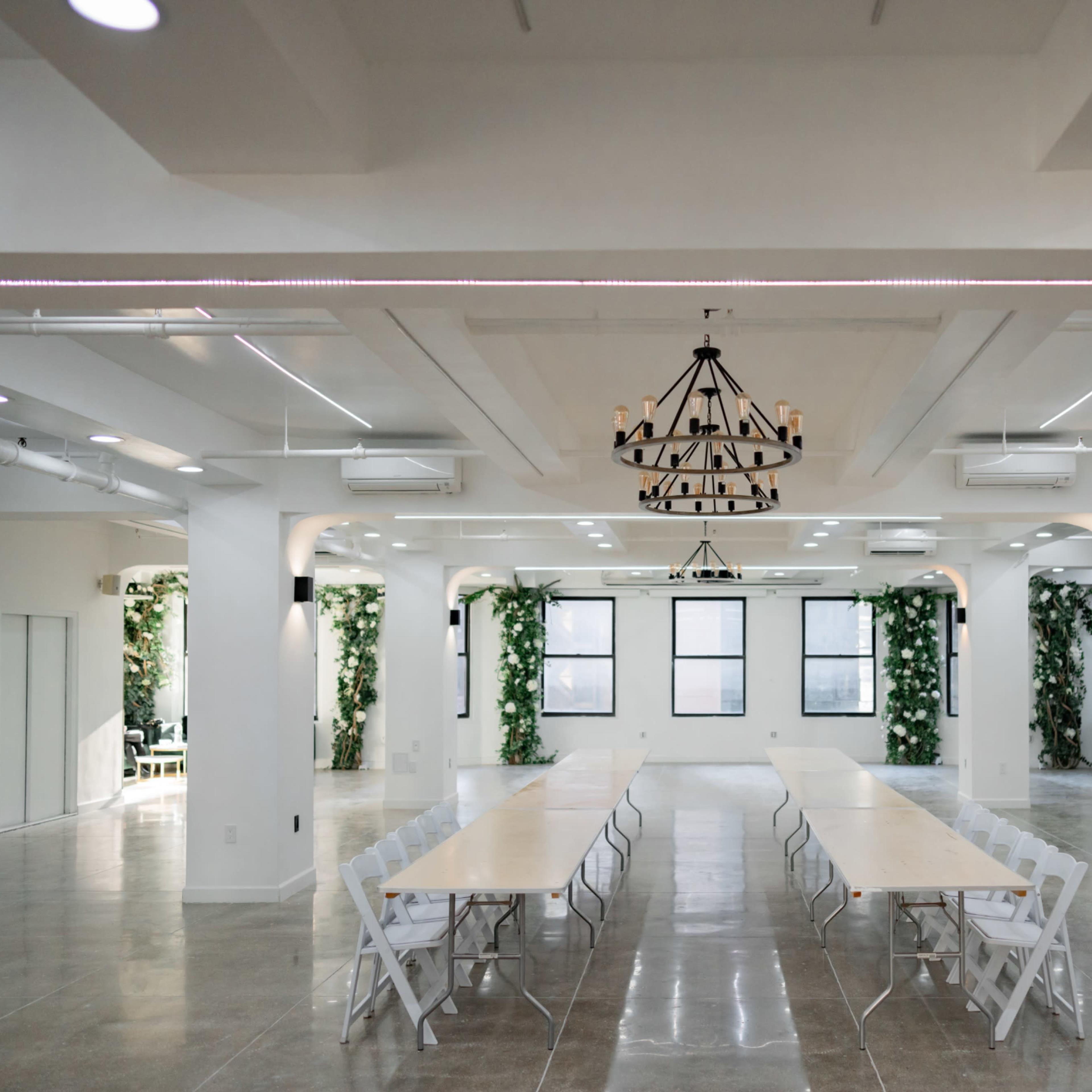 A spacious, modern meeting room with a long table set up in the center and greenery decorating the walls.