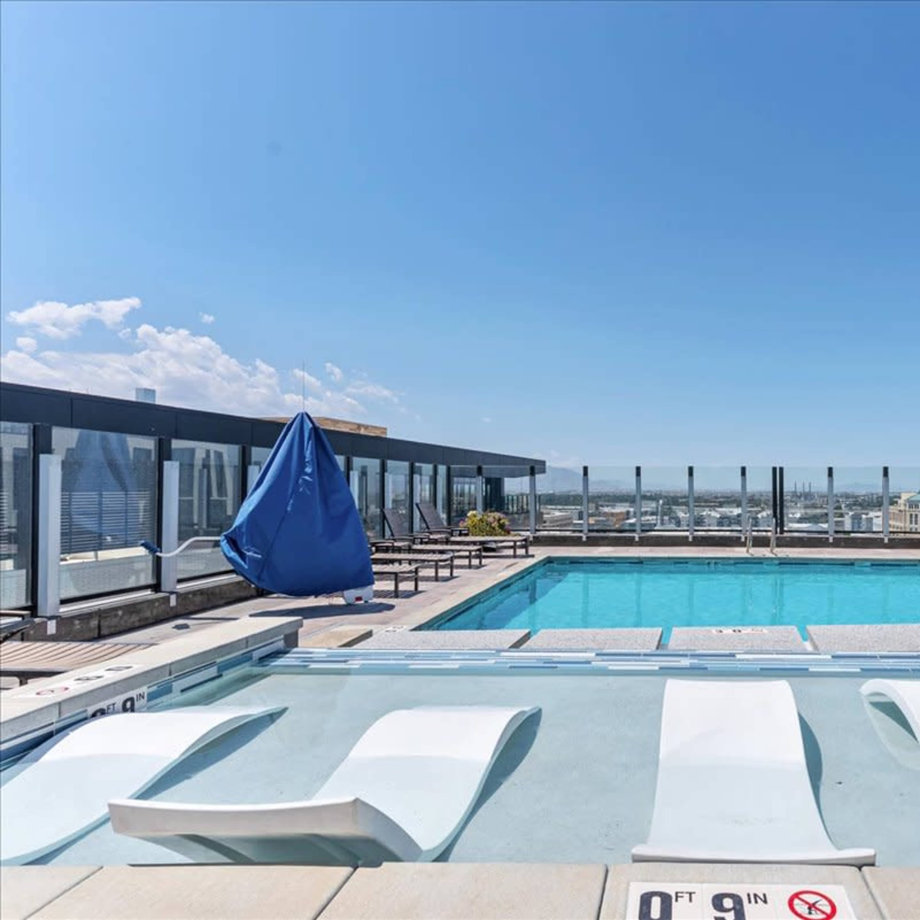 A rooftop pool is surrounded by modern buildings and clear blue skies.