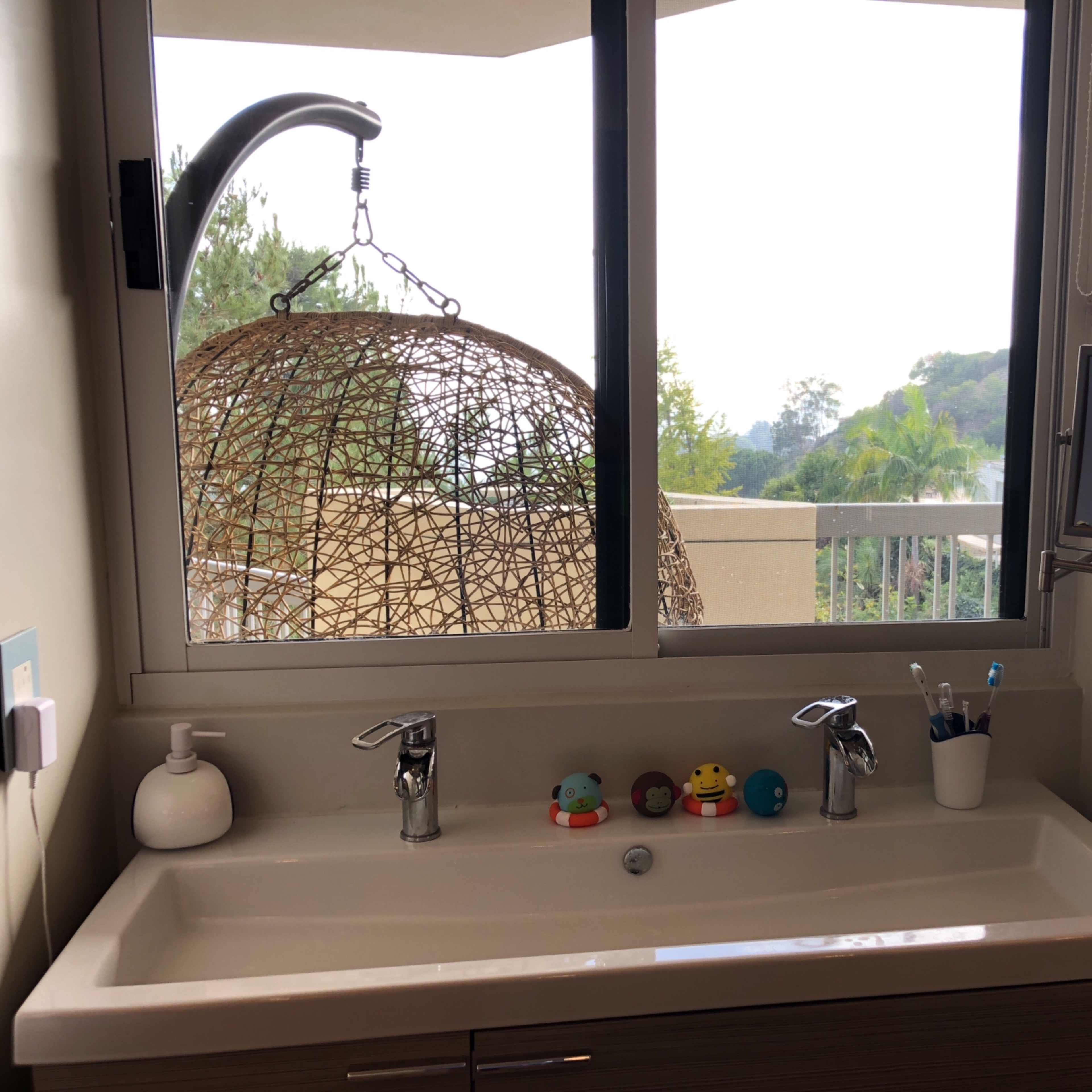 A bathroom sink with two faucets and decorative rubber ducks sits beneath a large window overlooking a scenic landscape.