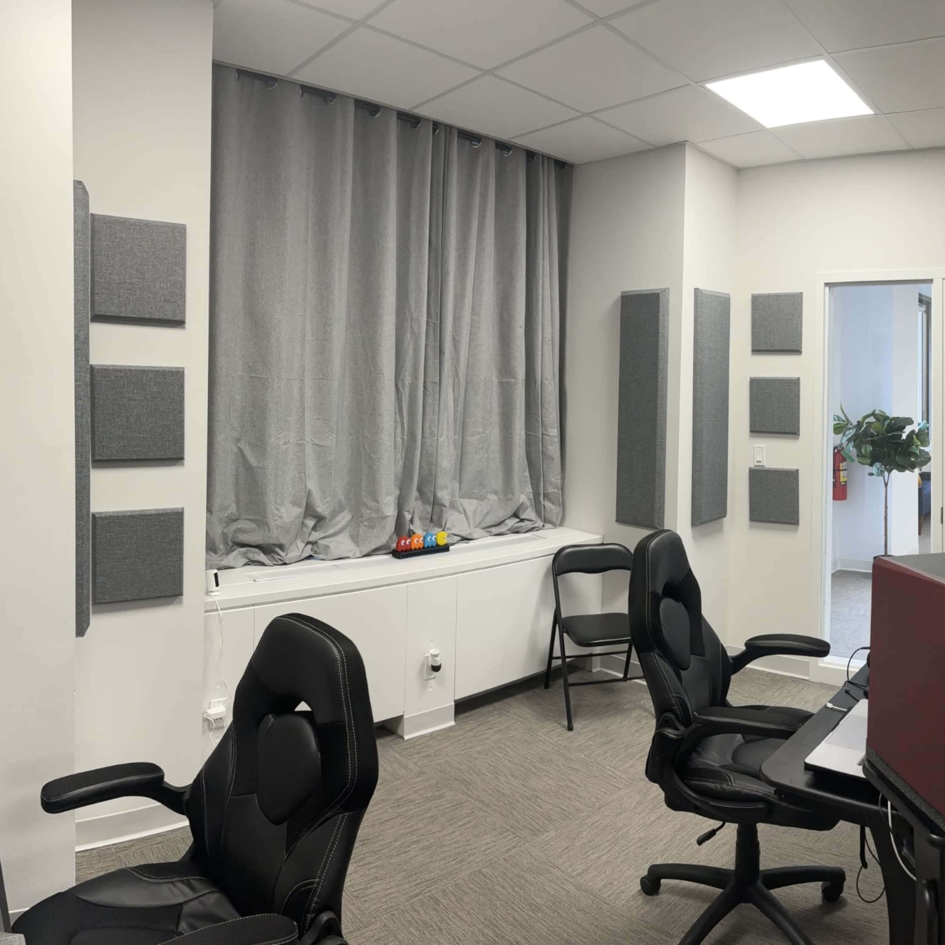 Two recording studio rooms, one with a large window and acoustic panels on the walls, and the other featuring a table and microphone setup.