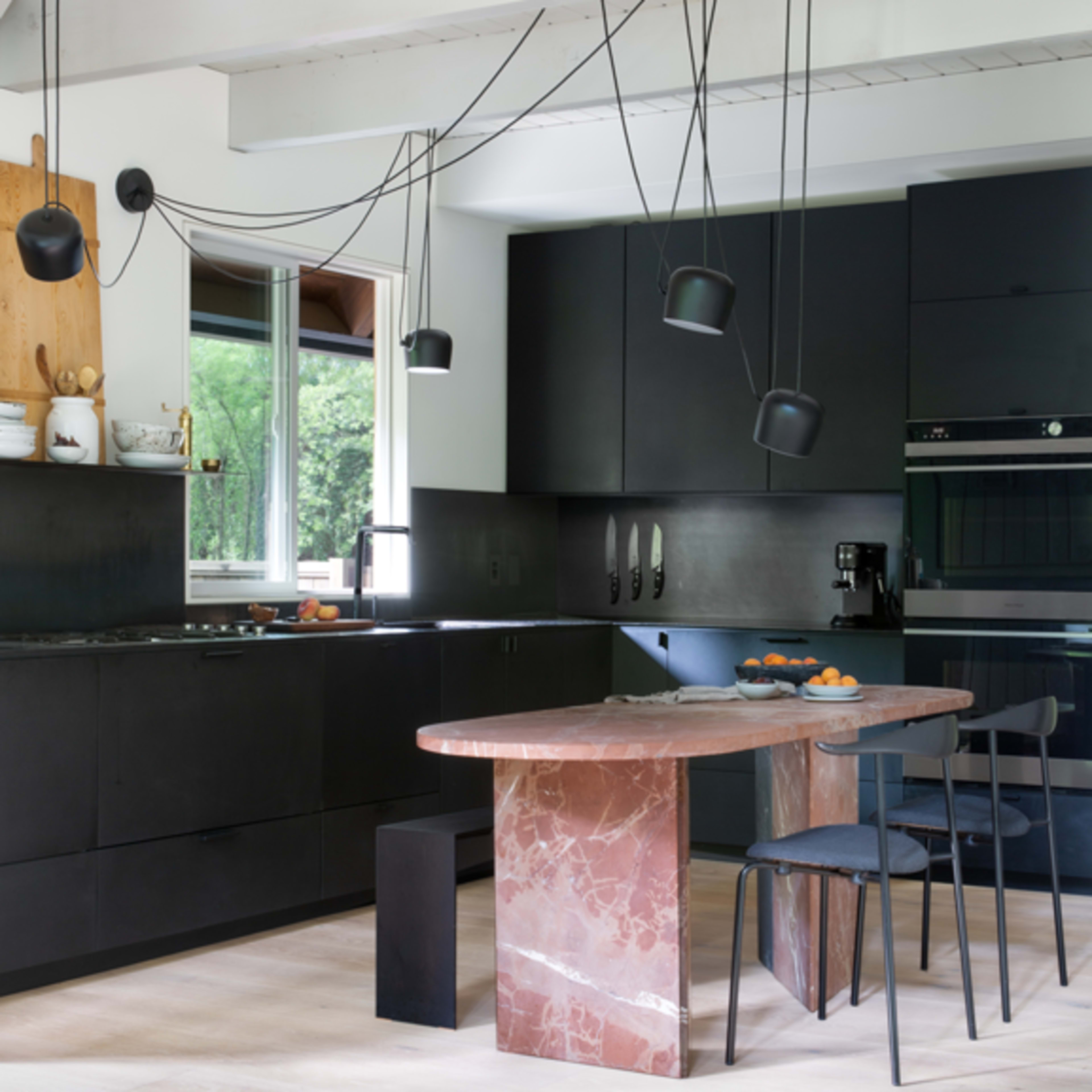 A modern kitchen featuring black cabinetry, a pink marble island, and pendant lights hanging from the ceiling.