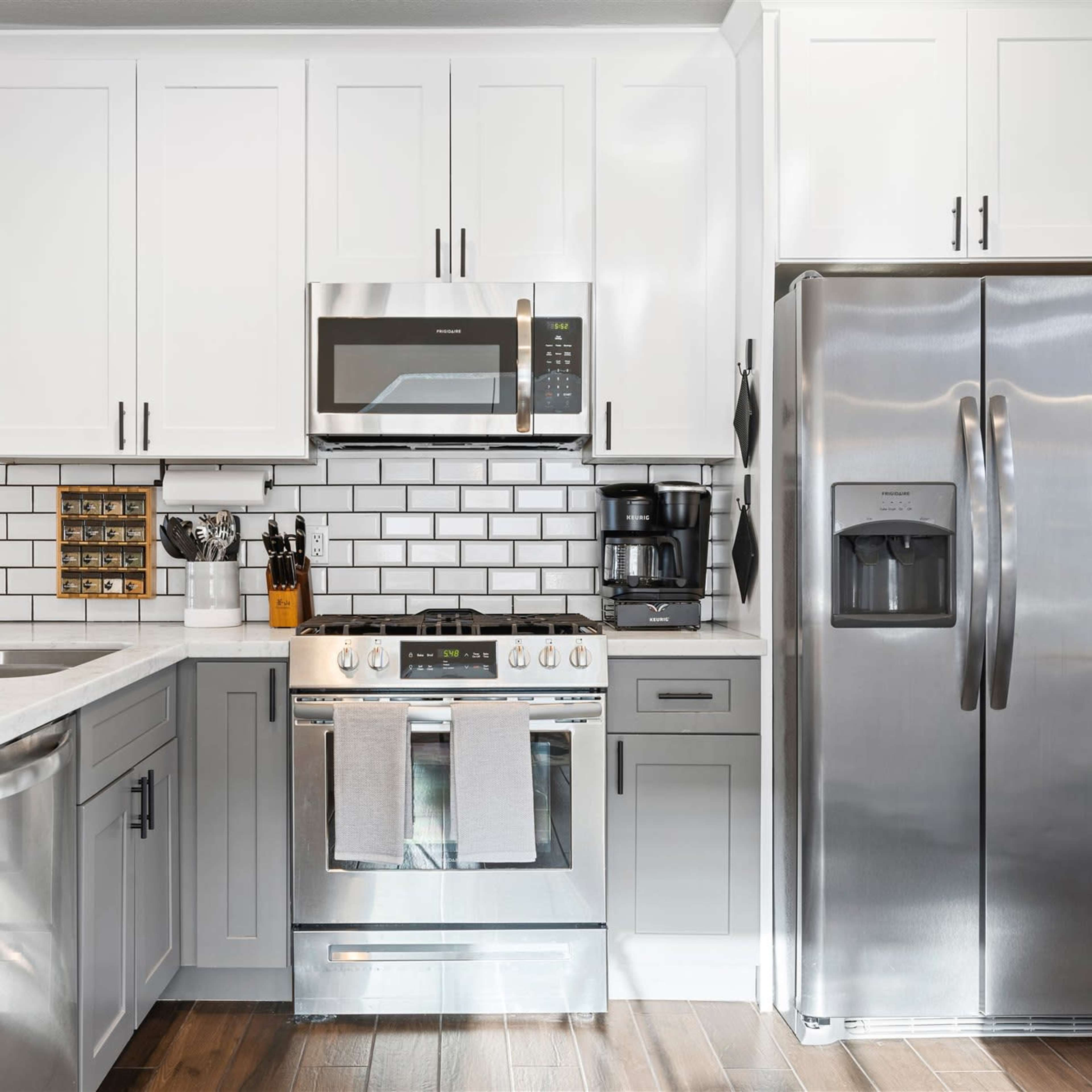 A modern kitchen with stainless steel appliances, white cabinetry, a tile backsplash, and a marble countertop.
