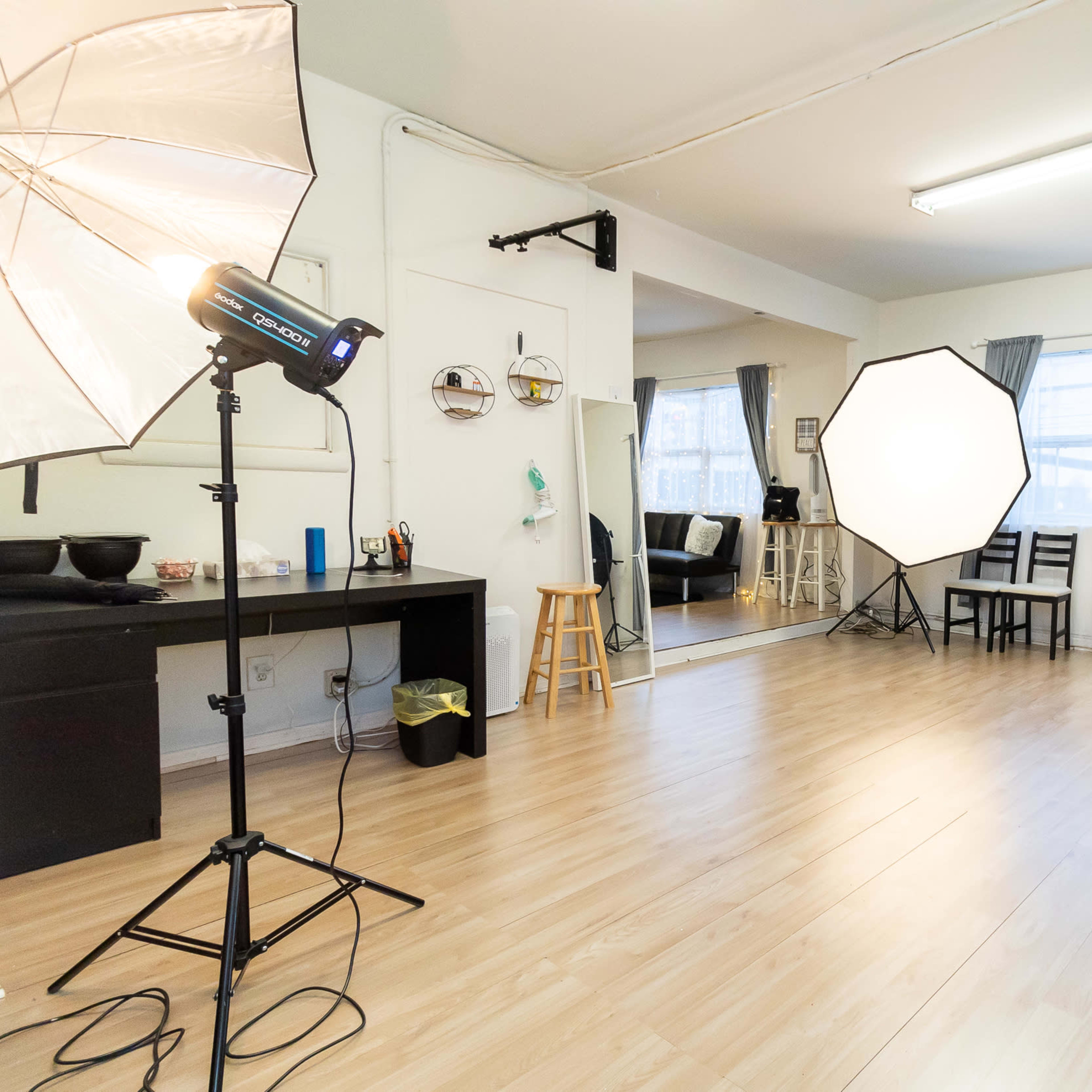 A photography studio with lighting equipment, a mirror, chairs, and wooden flooring.