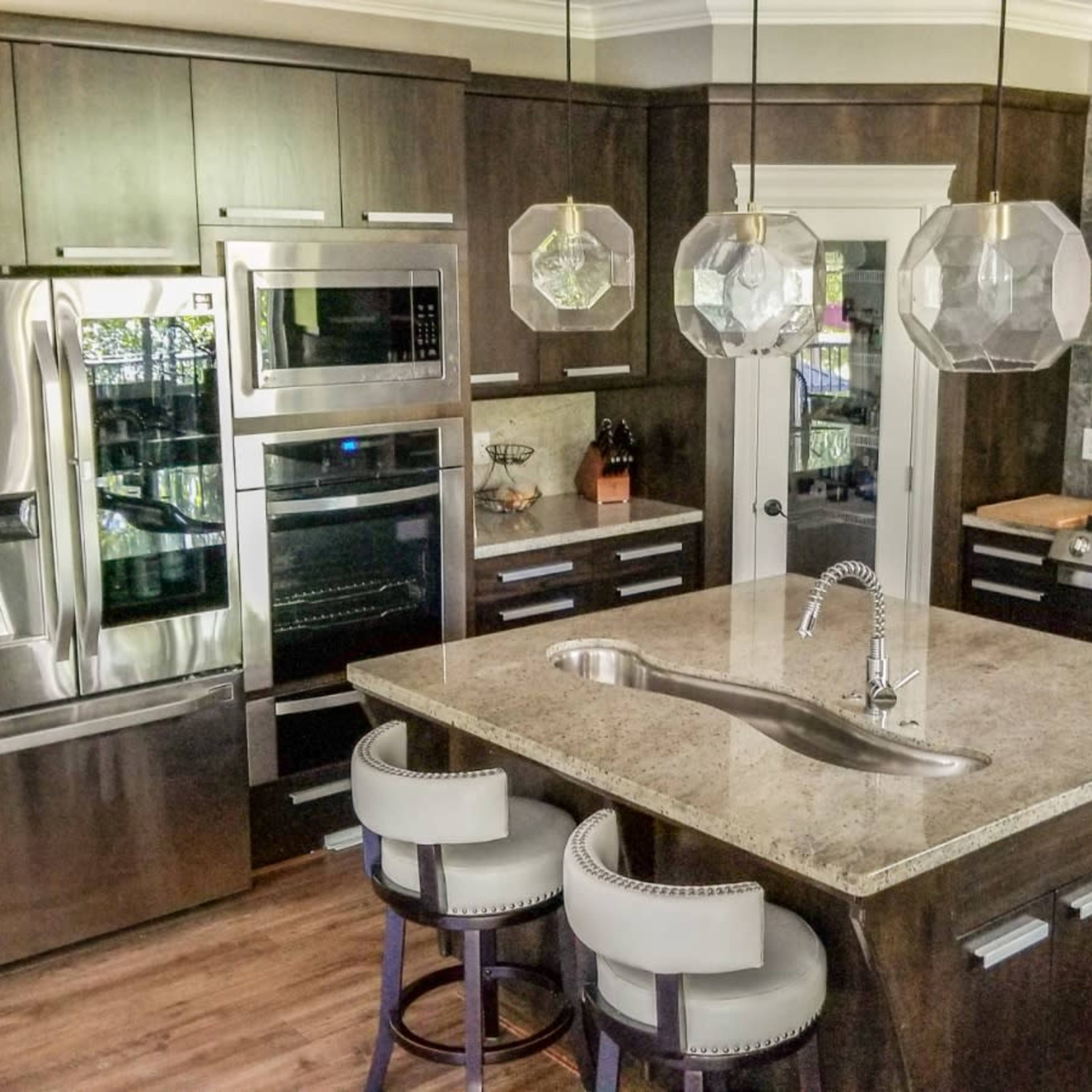 A modern kitchen featuring dark wood cabinets, stainless steel appliances, a large granite island with seating, and pendant lighting.