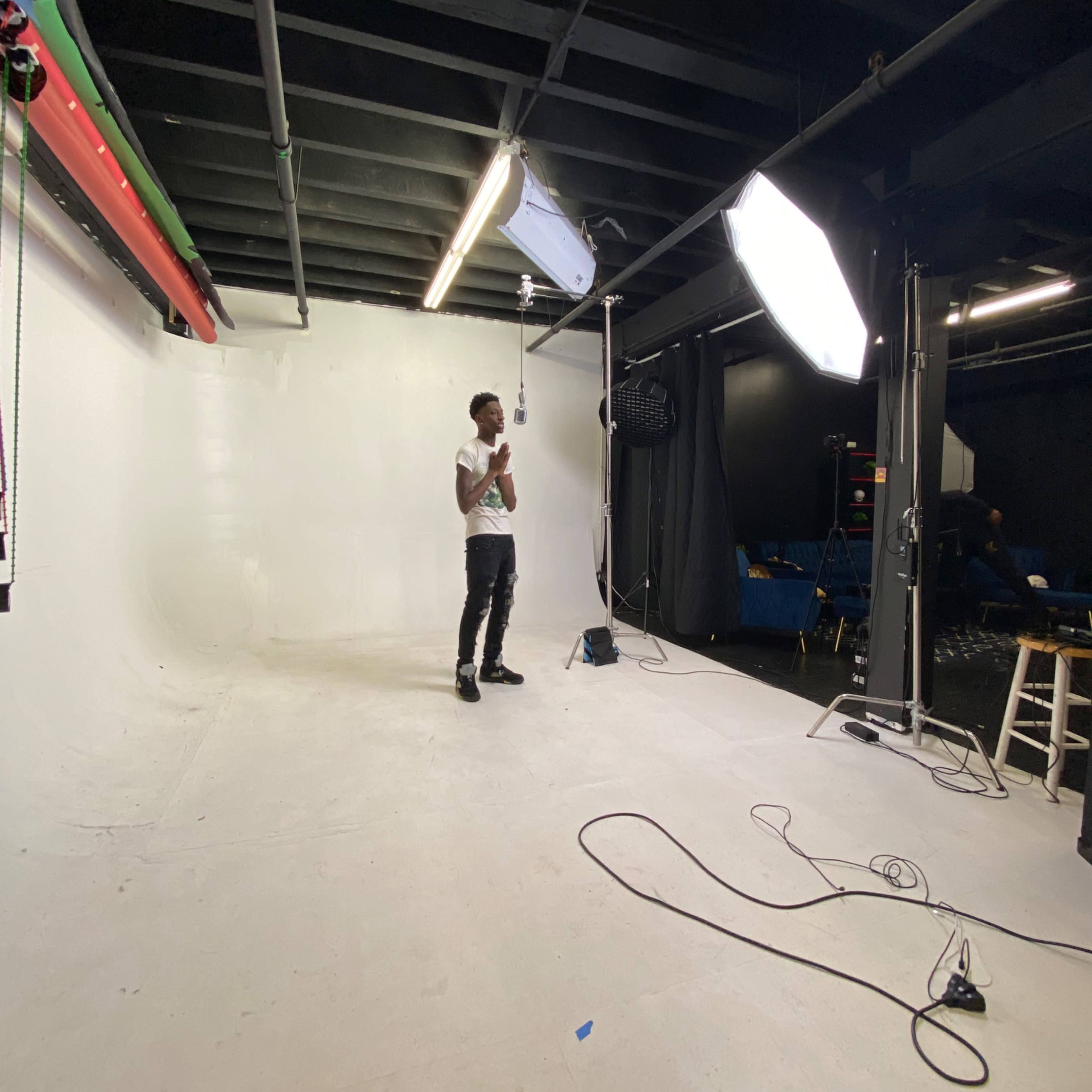 A person stands in a photography studio with a white backdrop and lighting equipment.