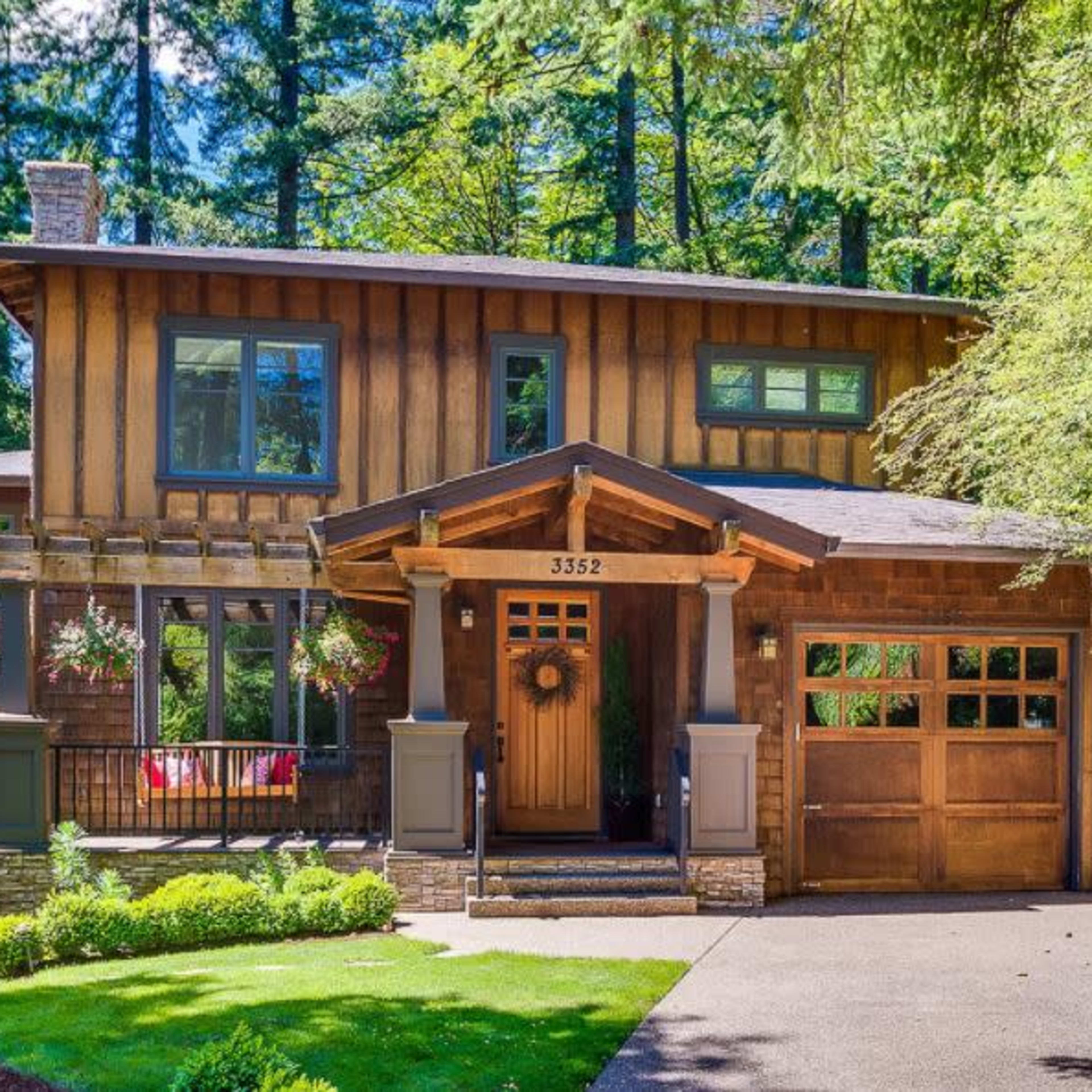 A two-story wooden house with a front porch, surrounded by trees and a neatly landscaped yard.