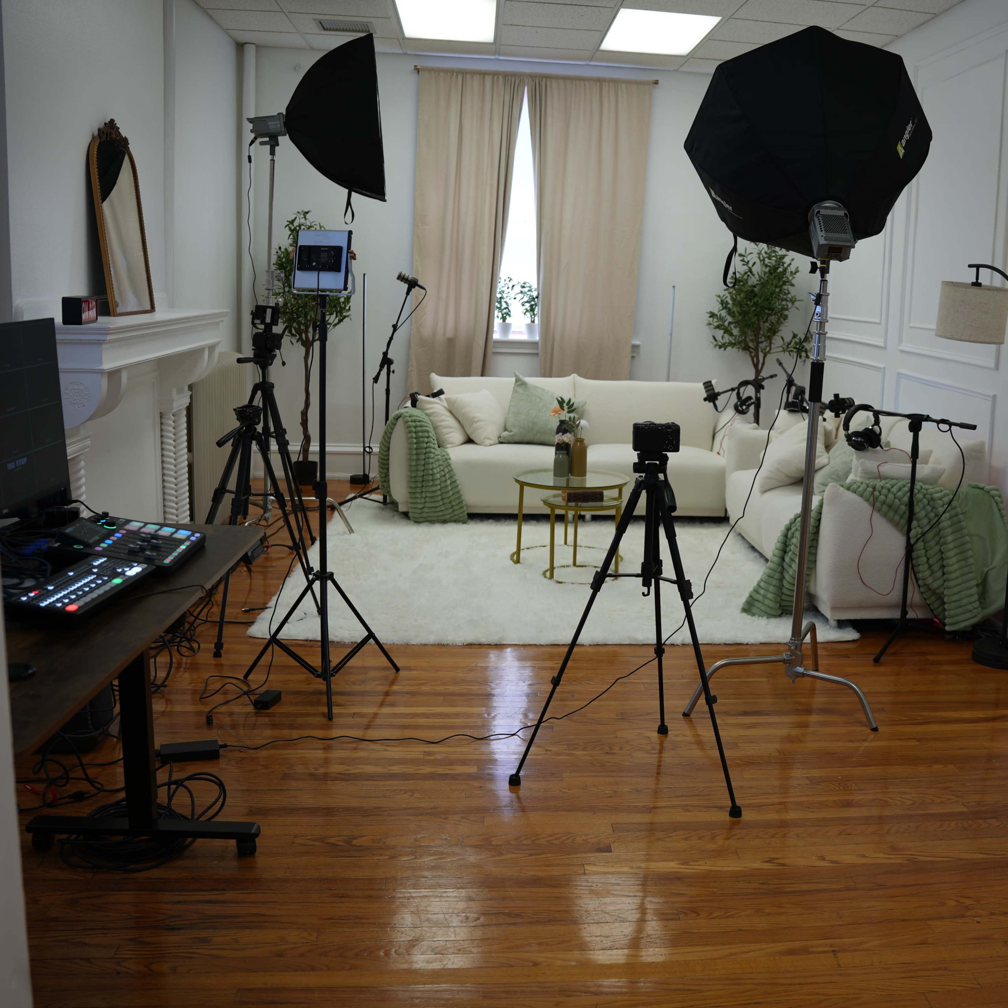 A well-lit studio setup featuring a sofa, decorative items, and multiple tripods with cameras and lighting equipment arranged around the room.