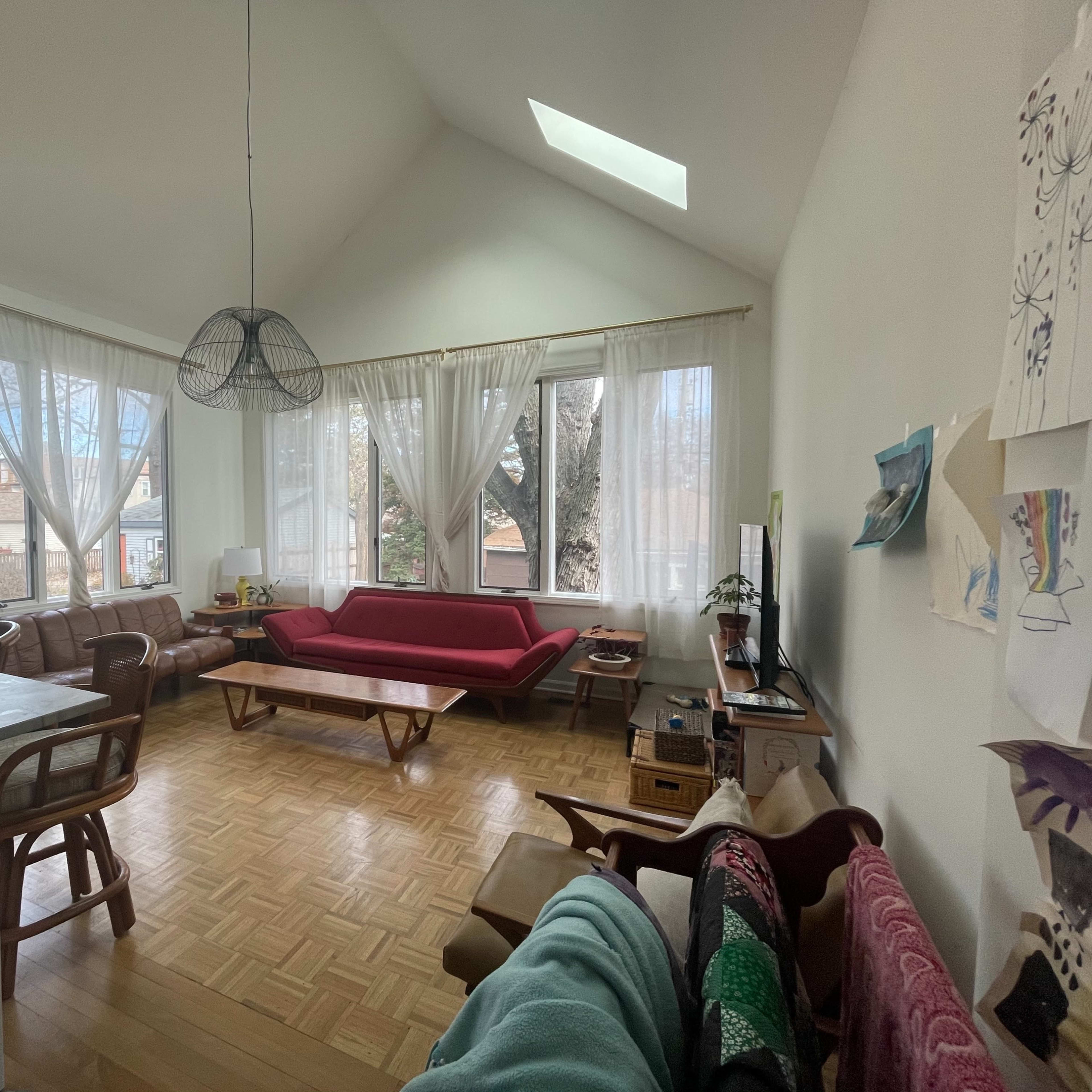 A spacious living room with large windows, a red sofa, wooden furniture, and a television.
