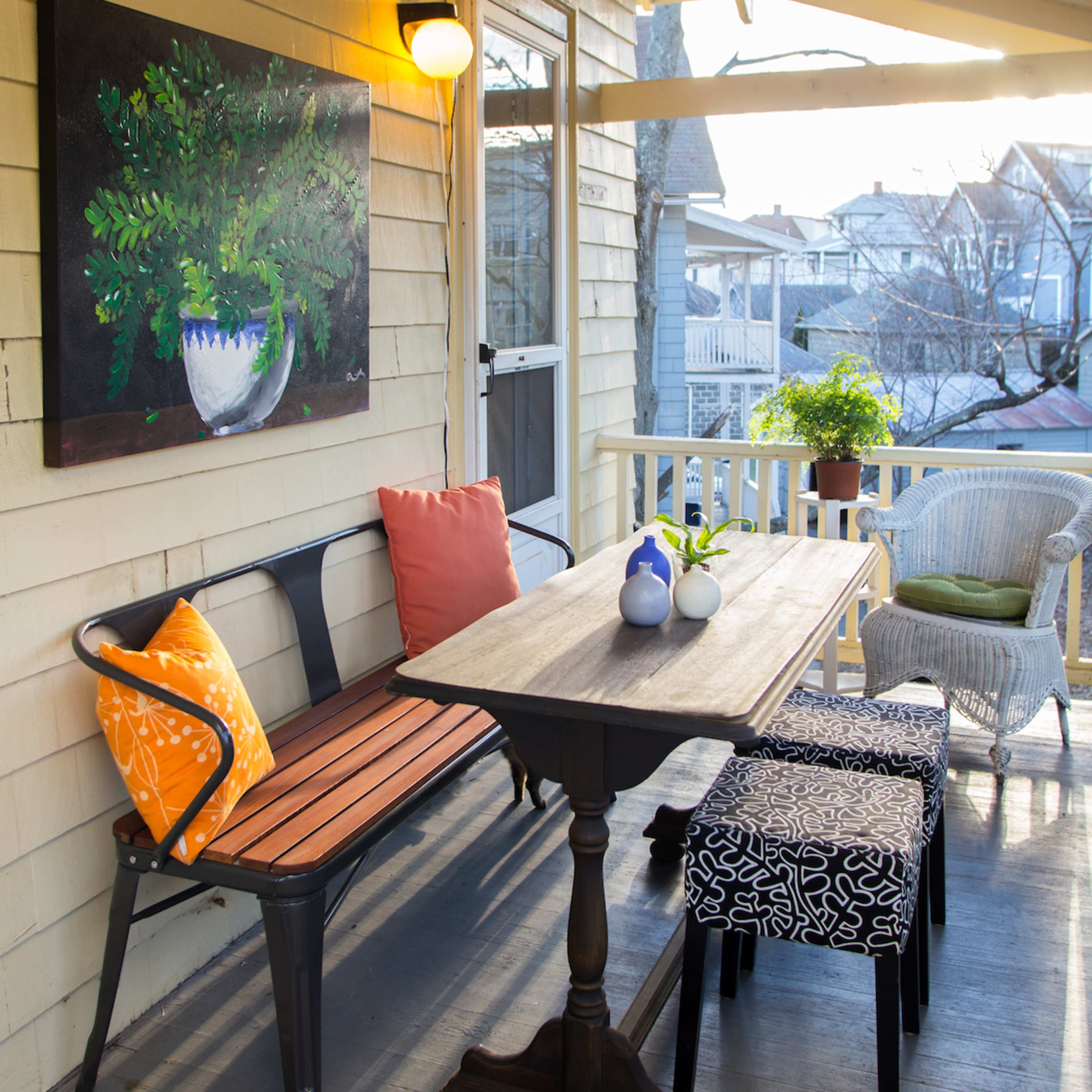 A cozy outdoor porch featuring a wooden table, colorful cushions on a bench, and string lights overhead.