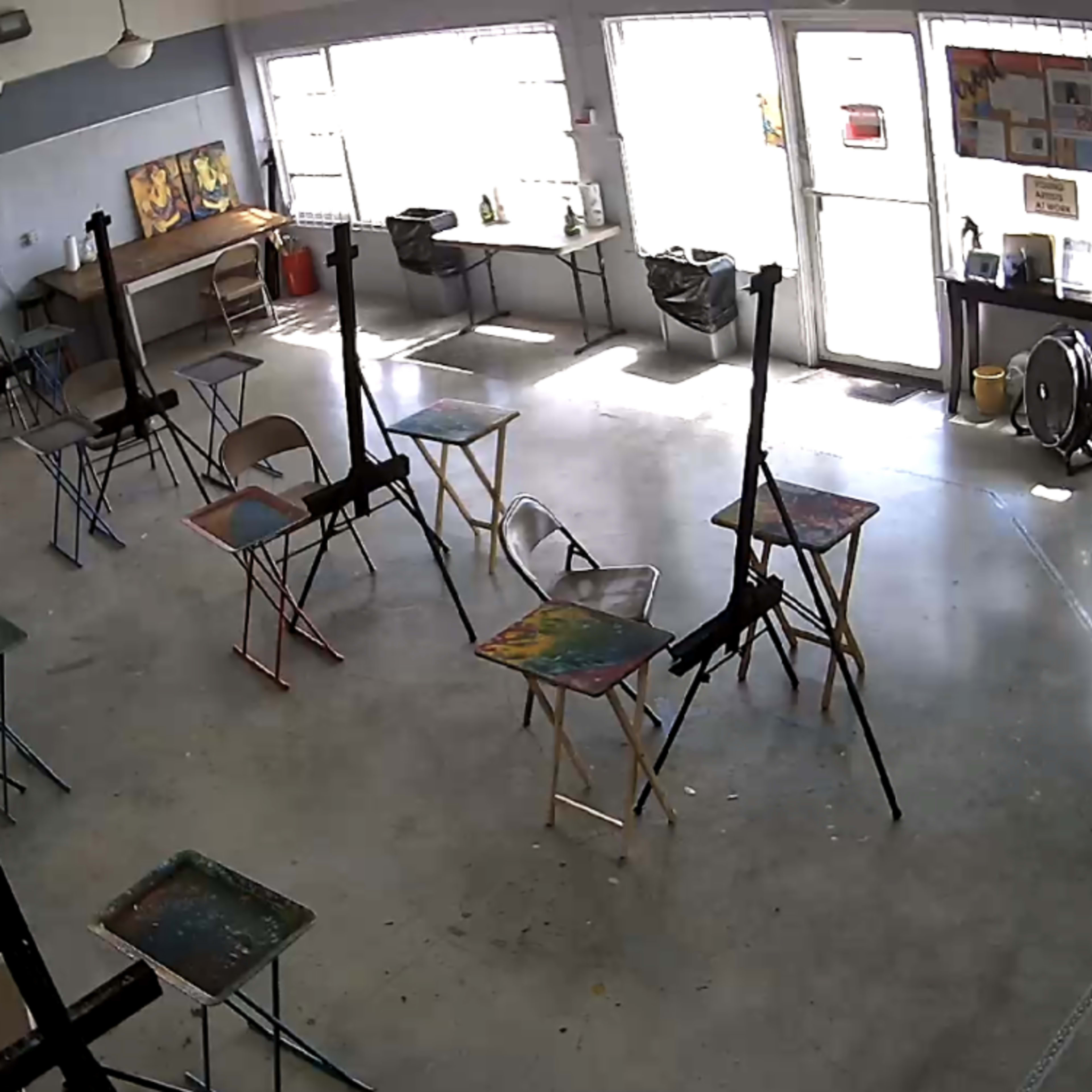 A spacious art studio with several easels and tables arranged in a well-lit room featuring large windows.