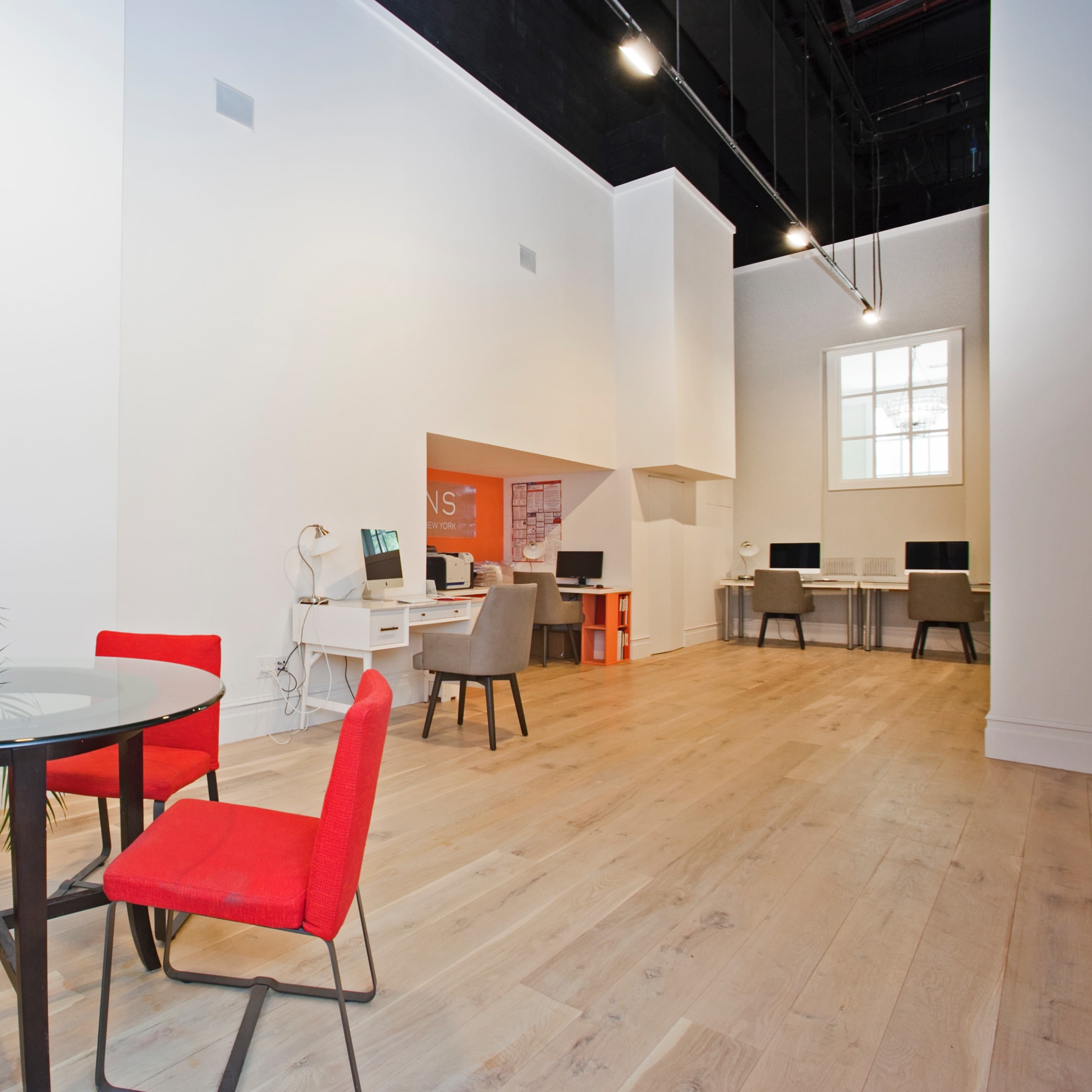 A modern office space with a glass table surrounded by red chairs, and computer workstations along the walls.