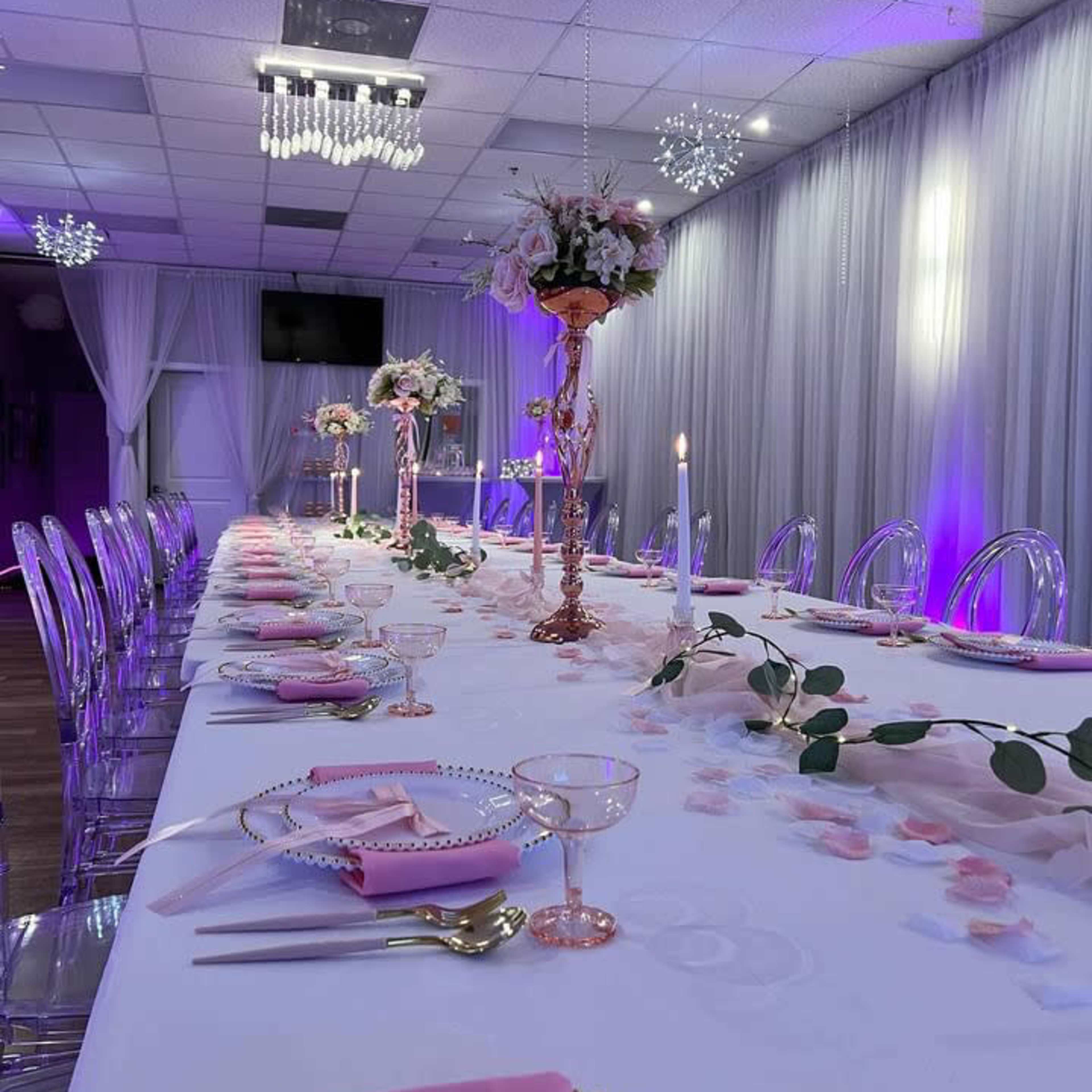 A long, elegantly set dining table is decorated with pink and gold tableware, floral centerpieces, and soft lighting.