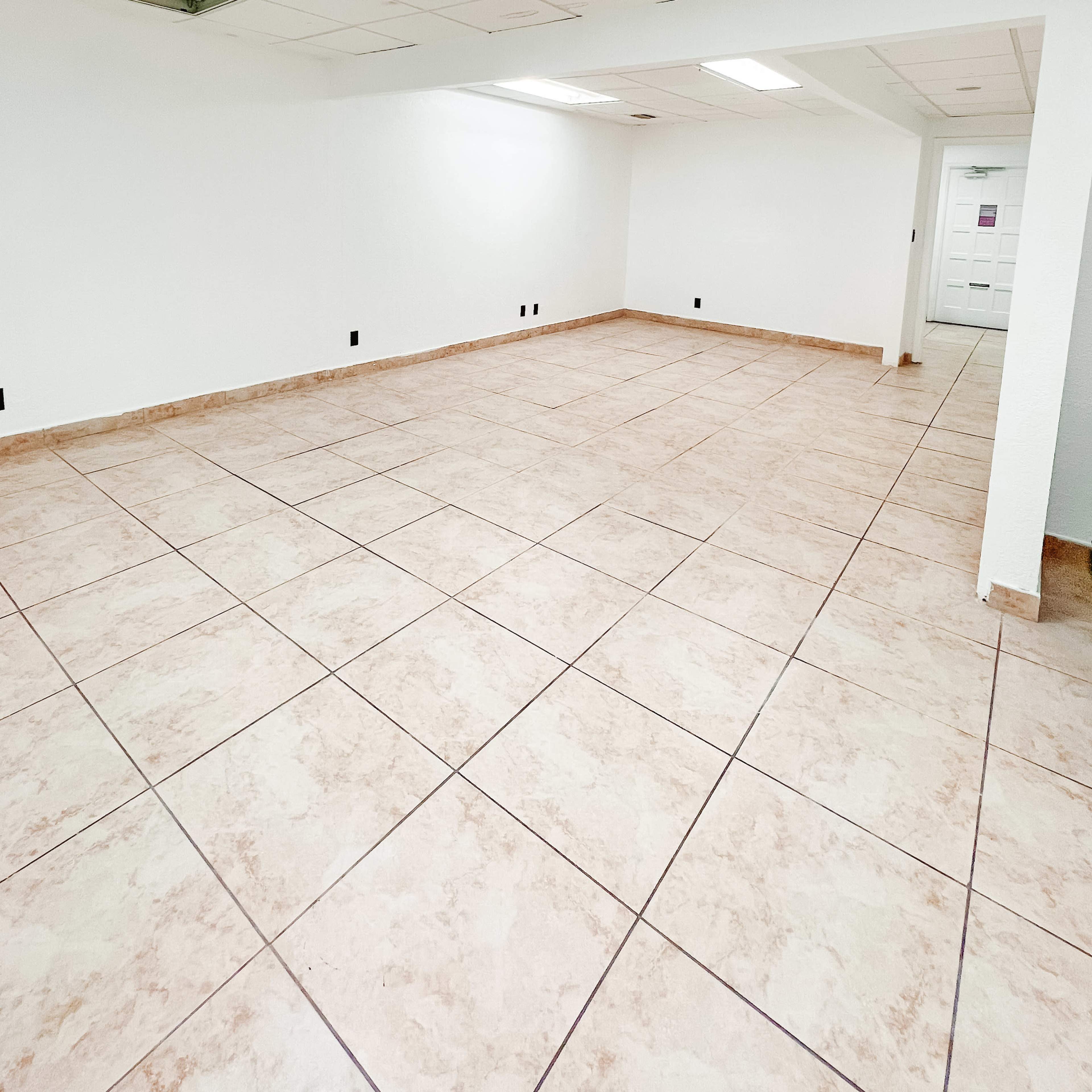 A spacious, empty room with tiled flooring and plain white walls.