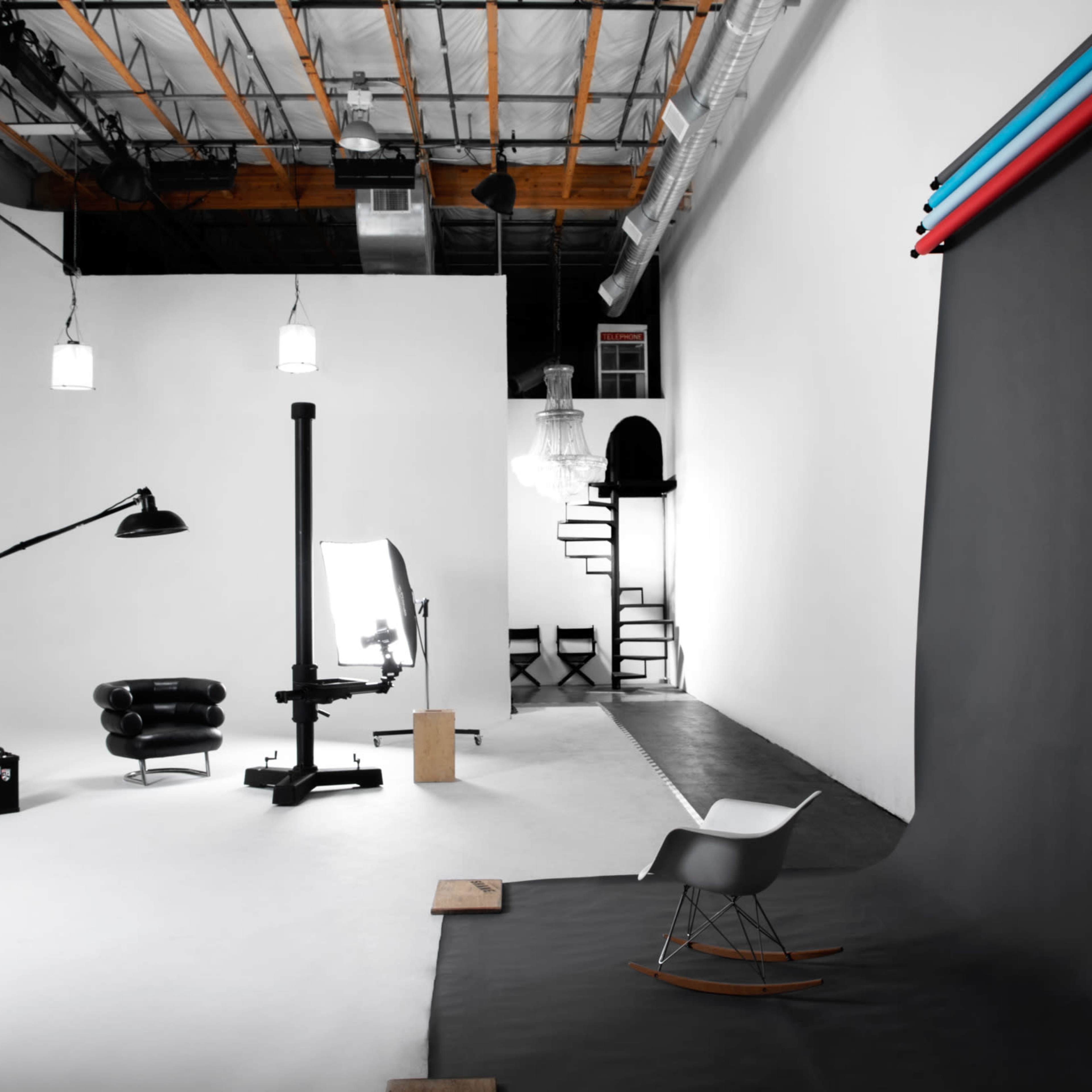 A photography studio with a backdrop, lighting equipment, and various props arranged in a spacious, minimalistic environment.
