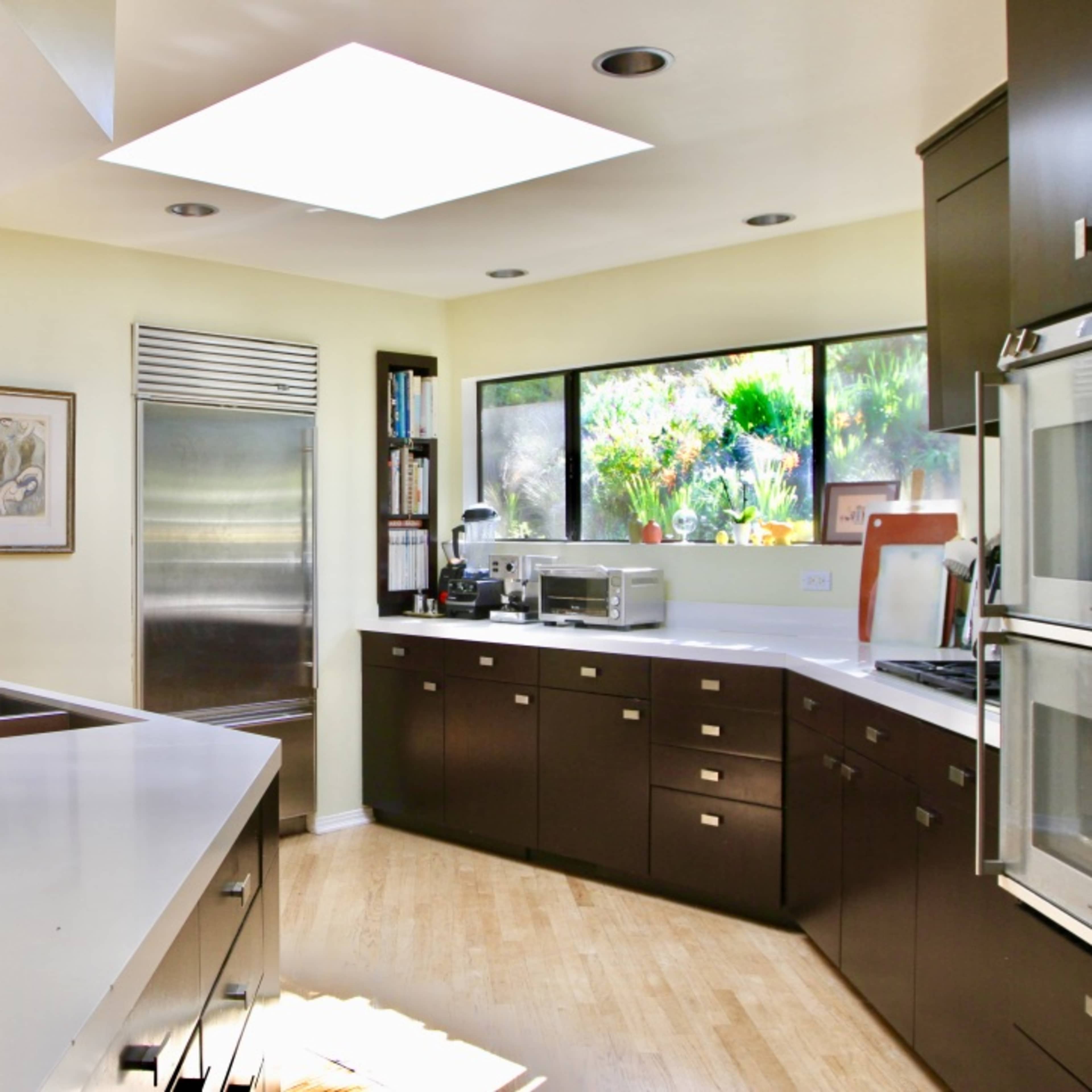A modern kitchen with sleek cabinetry, a skylight overhead, and large windows offering a view of greenery outside.