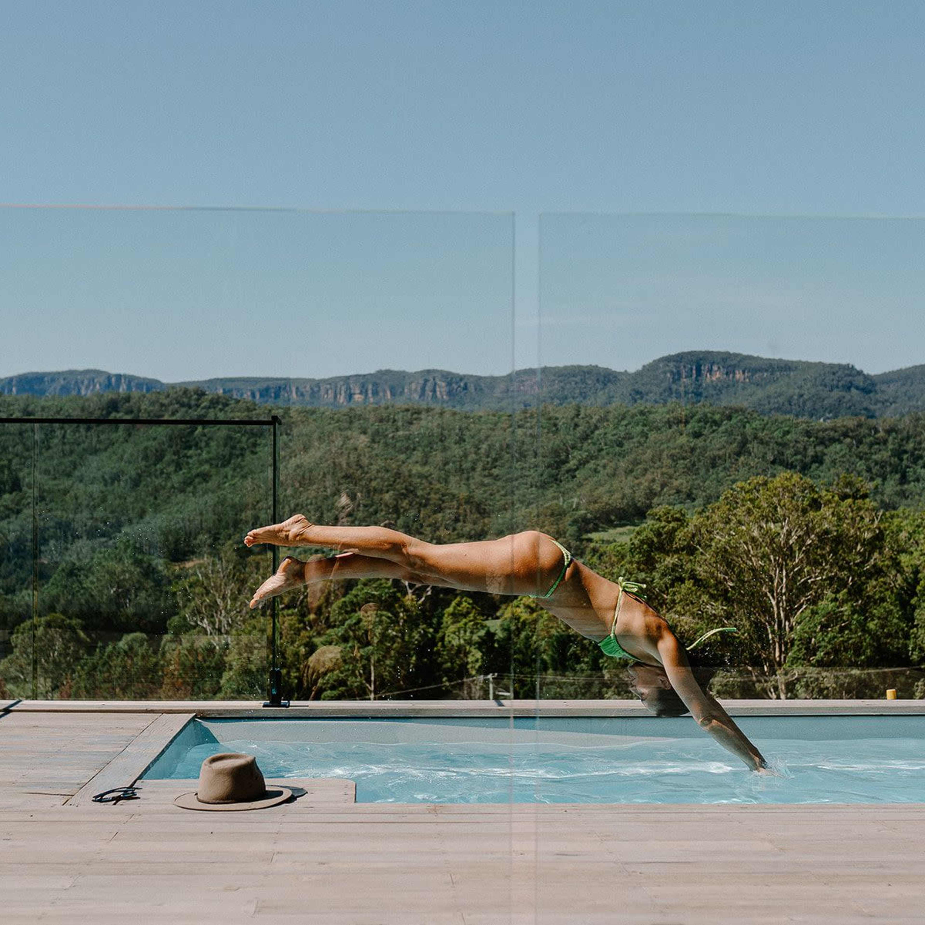 A person dives into a swimming pool surrounded by trees and mountains.