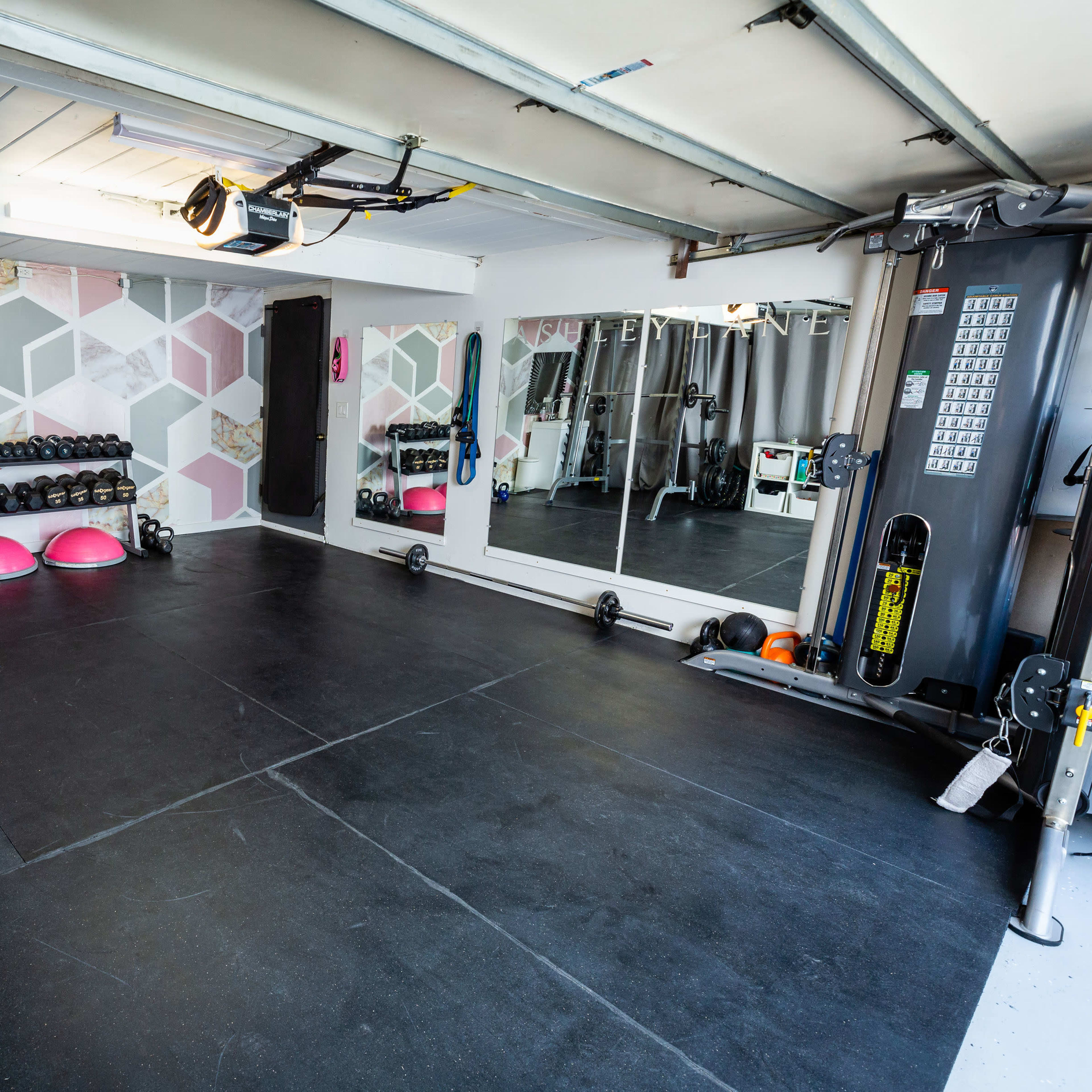 A gym interior with various weightlifting equipment, mirrors, and exercise balls arranged on a black rubber floor.