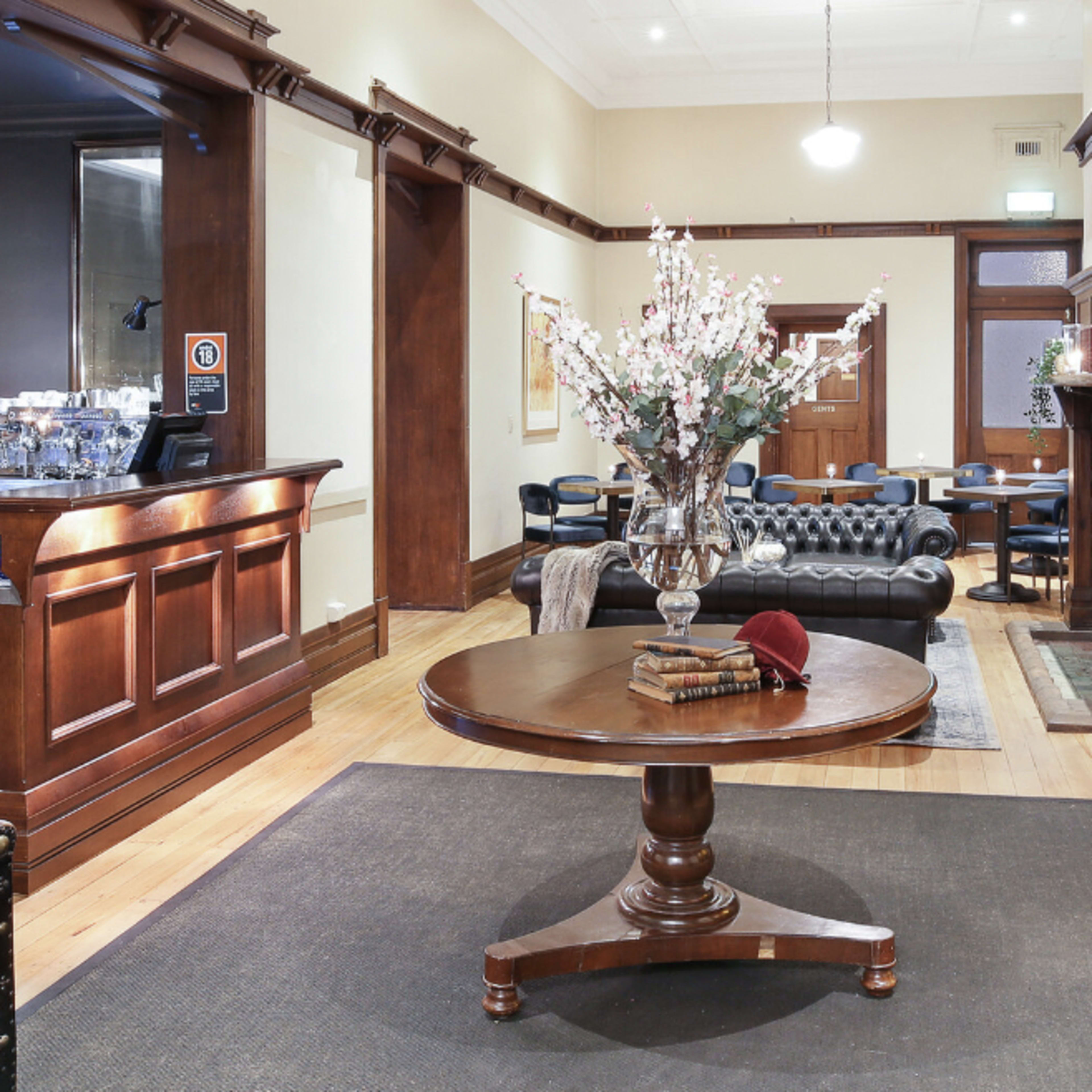 A lobby area featuring a round wooden table with a vase of flowers, surrounded by leather seating and a fireplace.