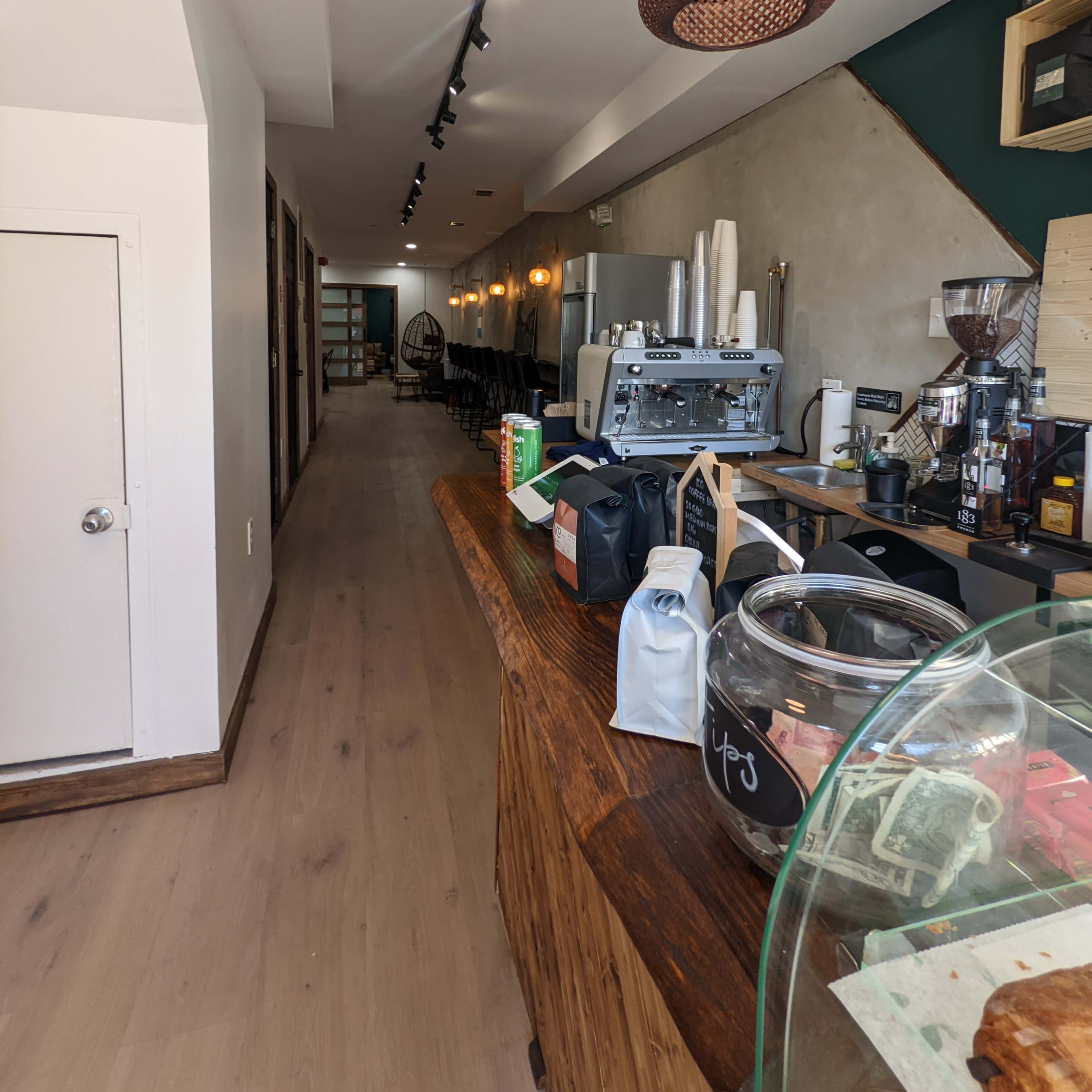 The interior of a café with a wooden counter, a coffee machine, and a long hallway leading to additional seating areas.