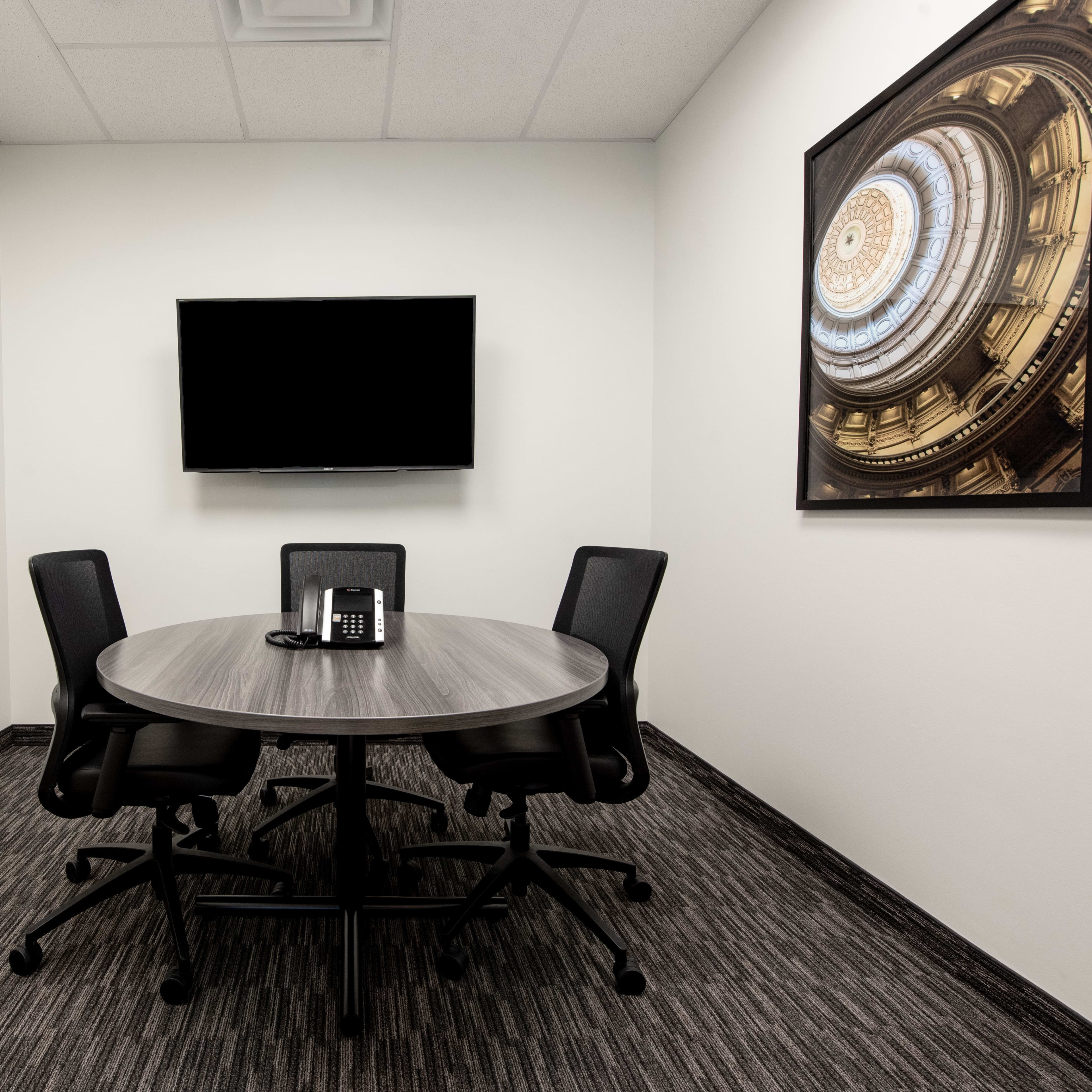 A small conference room features a round table with four chairs, a telephone, and two framed artworks on the walls.