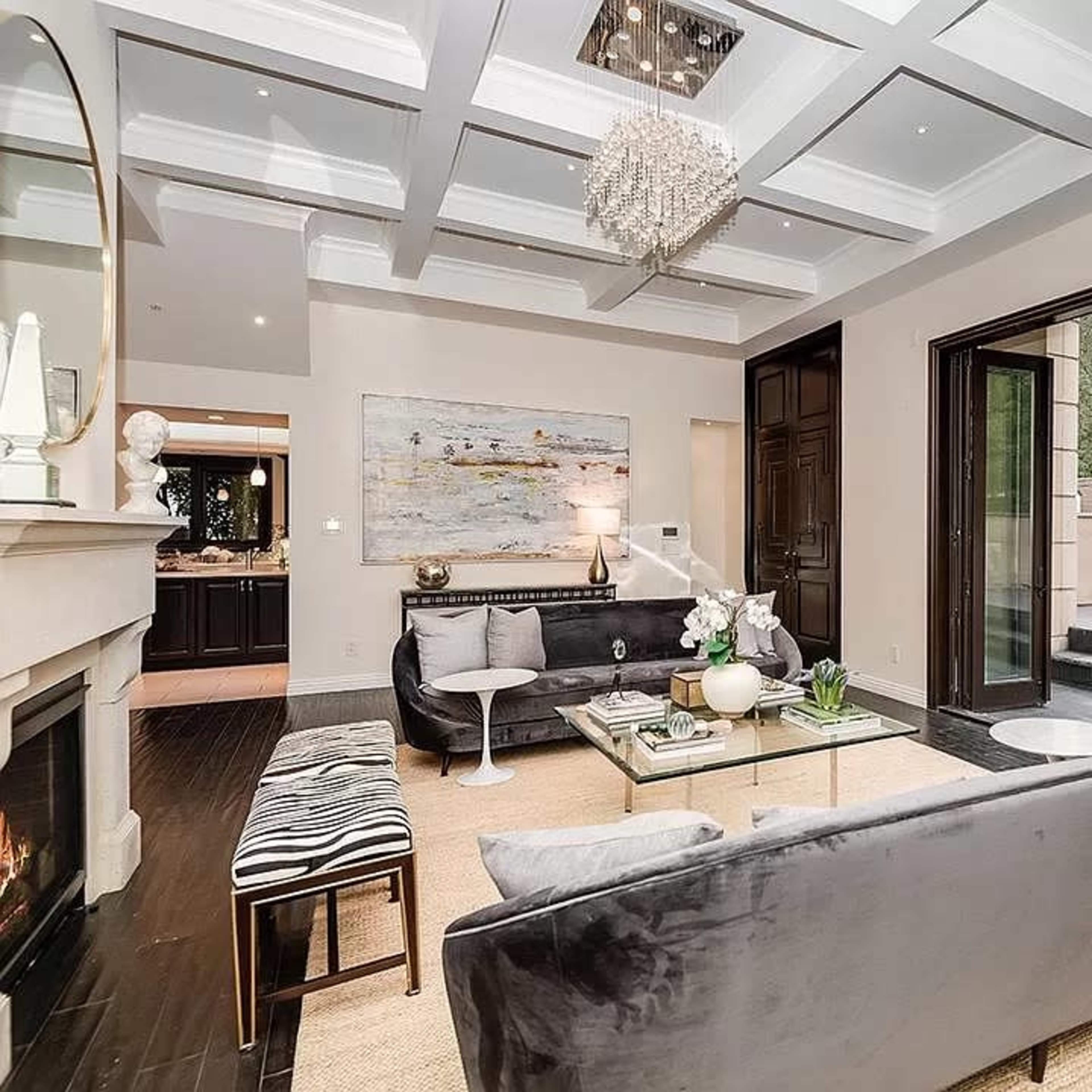 The living room features a gray sofa, a glass coffee table, and large sliding doors that open to an outdoor patio with a garden view.