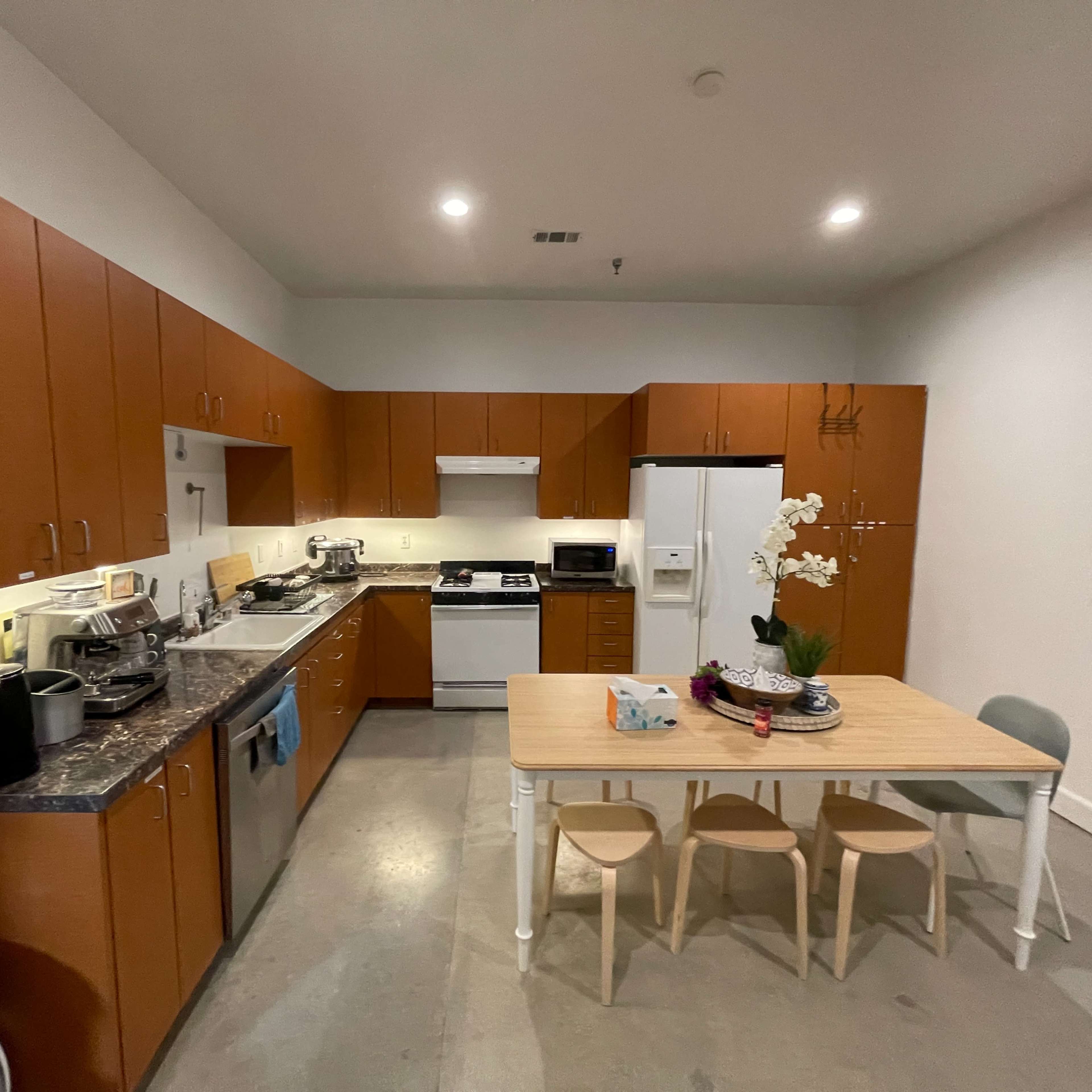 A modern kitchen features wooden cabinetry, stainless steel appliances, and a dining table with chairs.