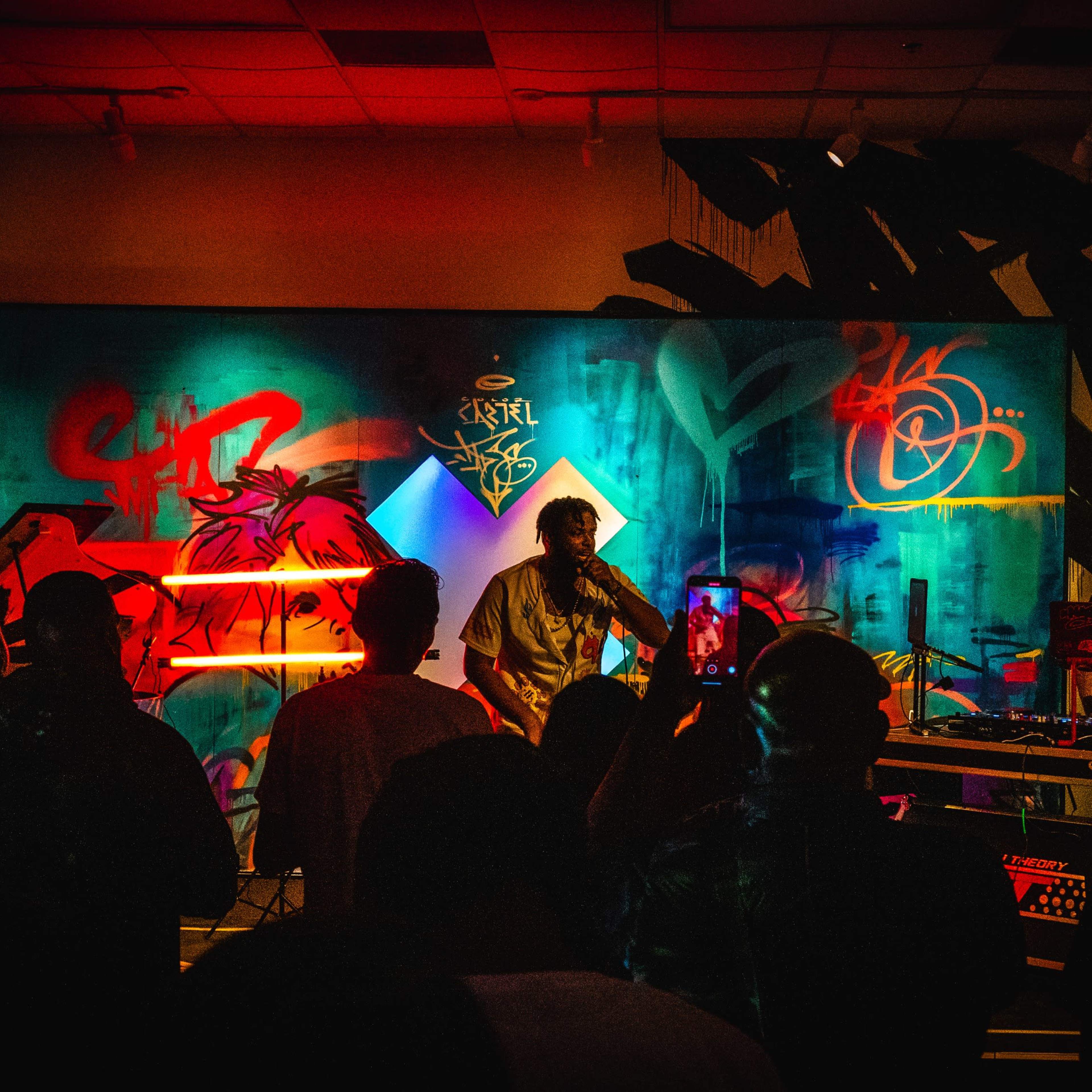 A musician performs on stage in front of a crowd, with vibrant graffiti artwork displayed behind them.
