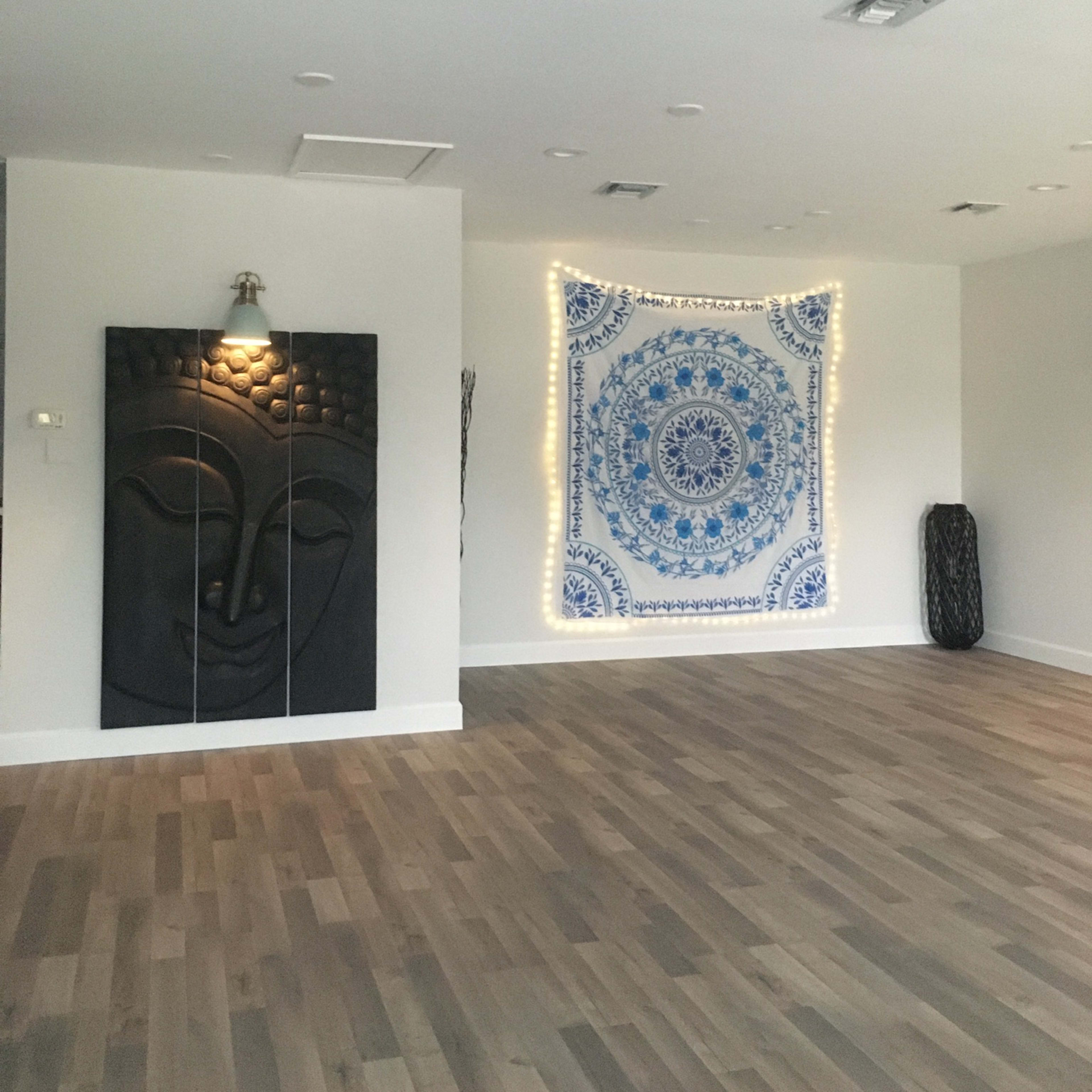 A spacious room with wooden flooring, featuring a wall tapestry and a large decorative wall panel with a Buddha face.