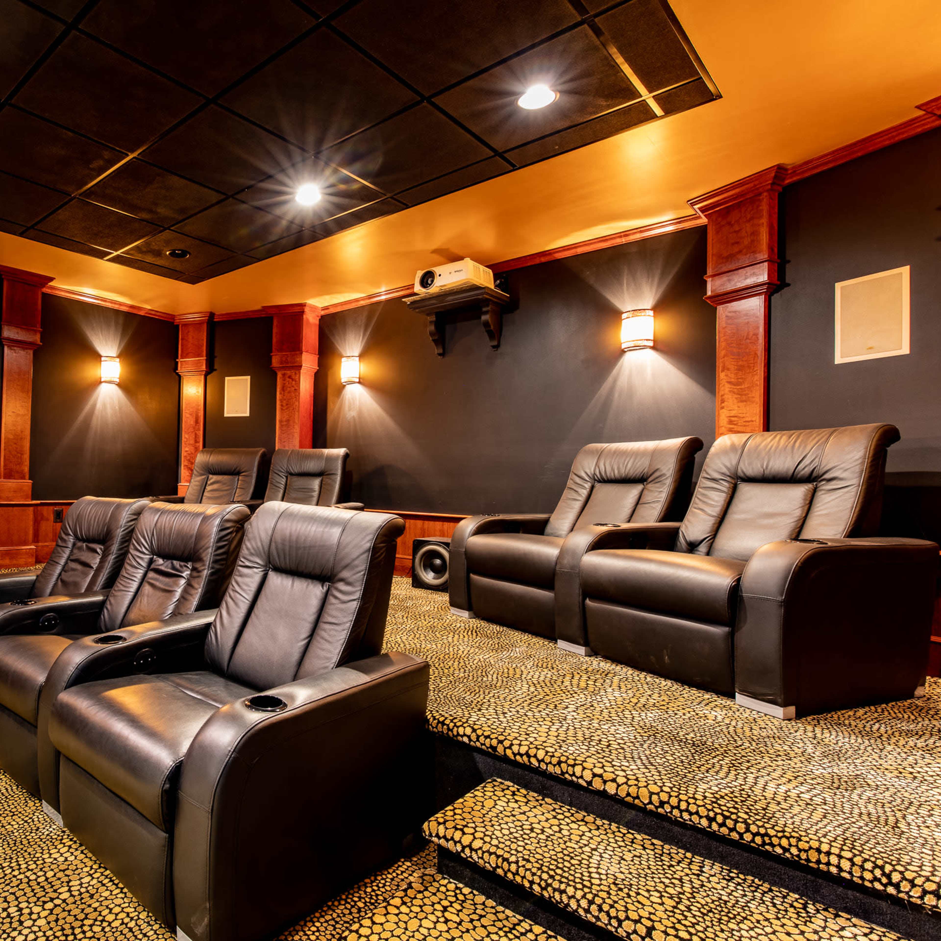 A dimly lit home theater with dark leather recliners arranged in front of a projector screen.