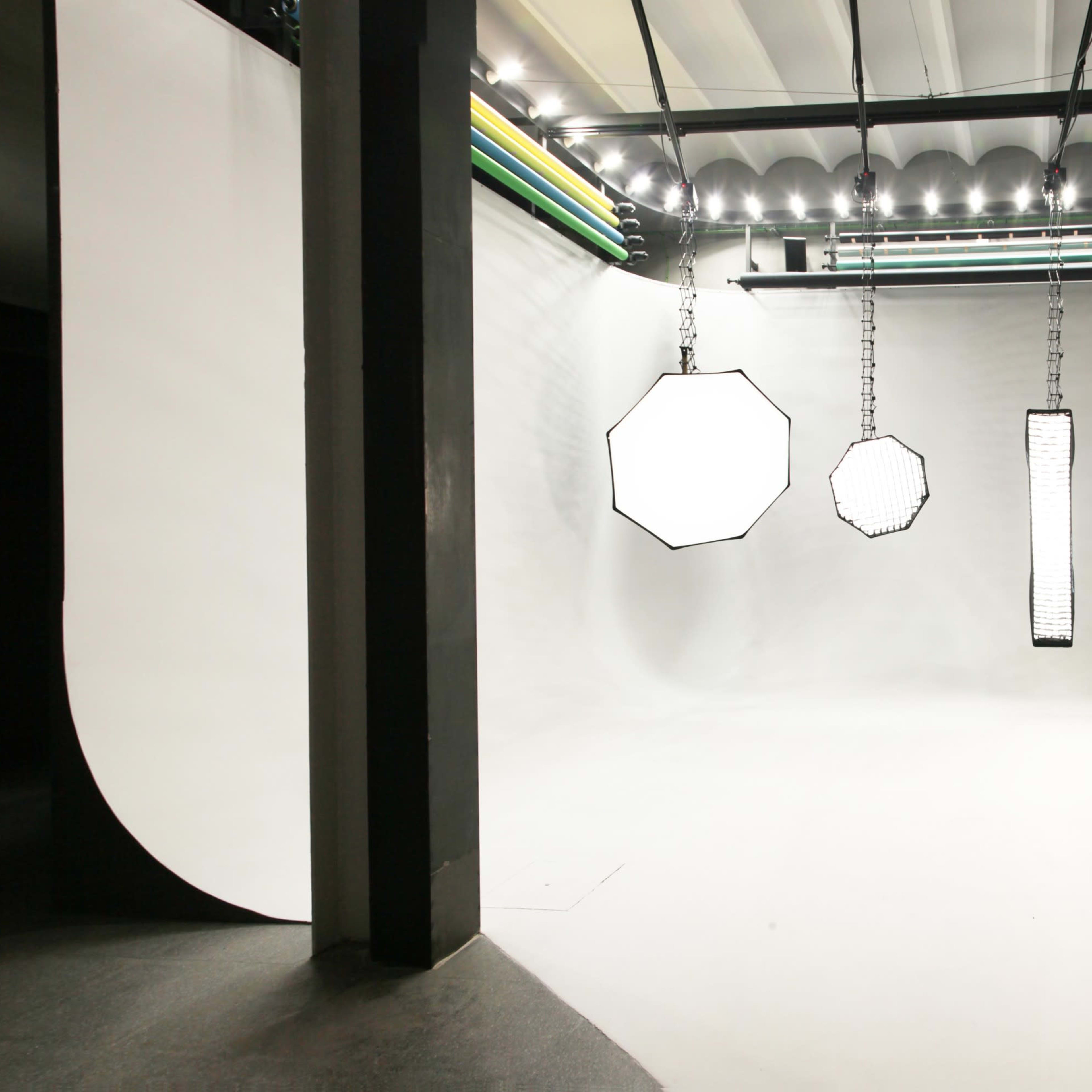 A photography studio features a seamless white backdrop with various hanging light sources.