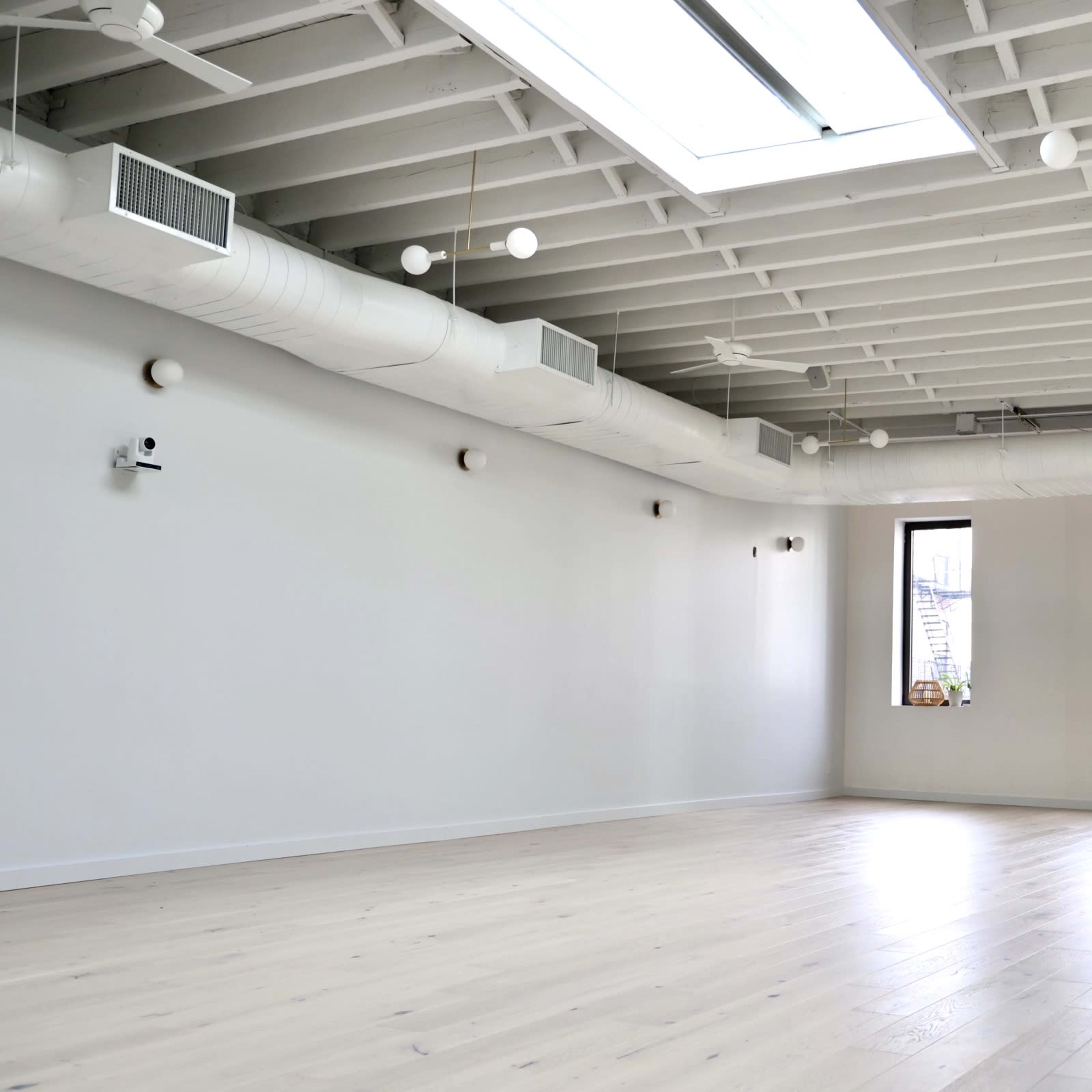 A spacious, uncluttered room with white walls, wooden floors, and large windows.