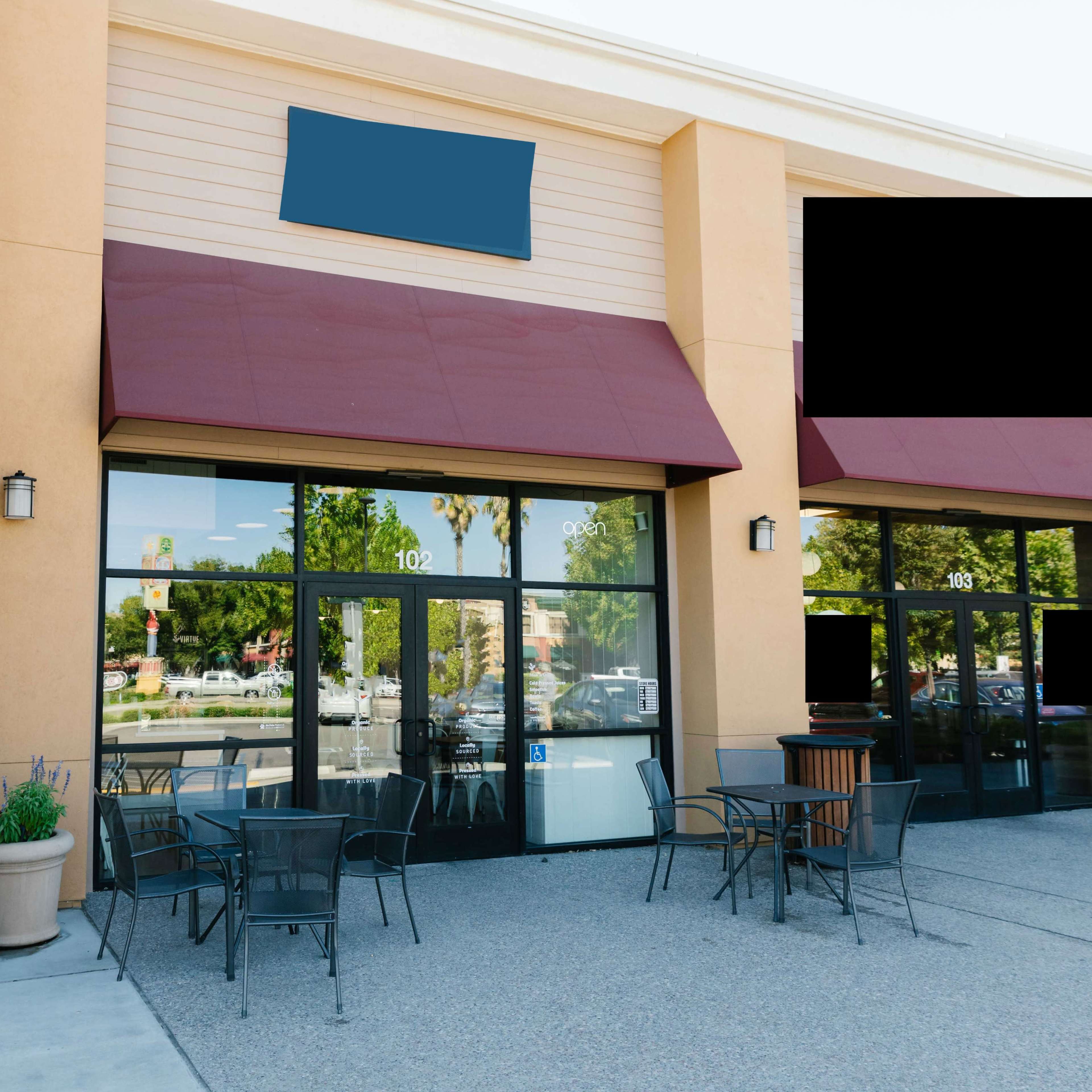 A storefront with a maroon awning, glass doors, and a small seating area with black chairs and tables outside.