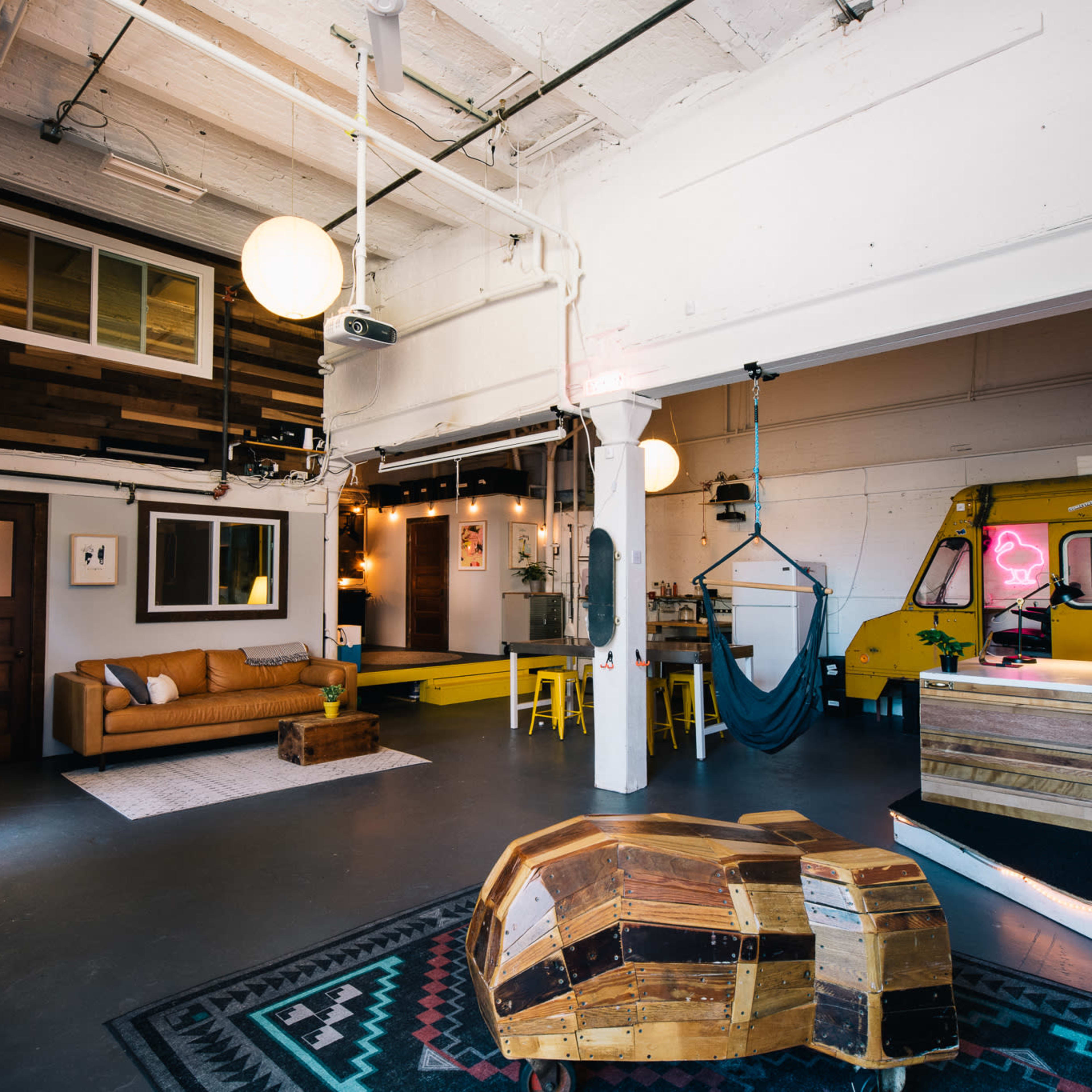An open-plan workspace featuring a cozy sitting area with a couch, a small reception area with a vintage vehicle, and a clothing display rack.