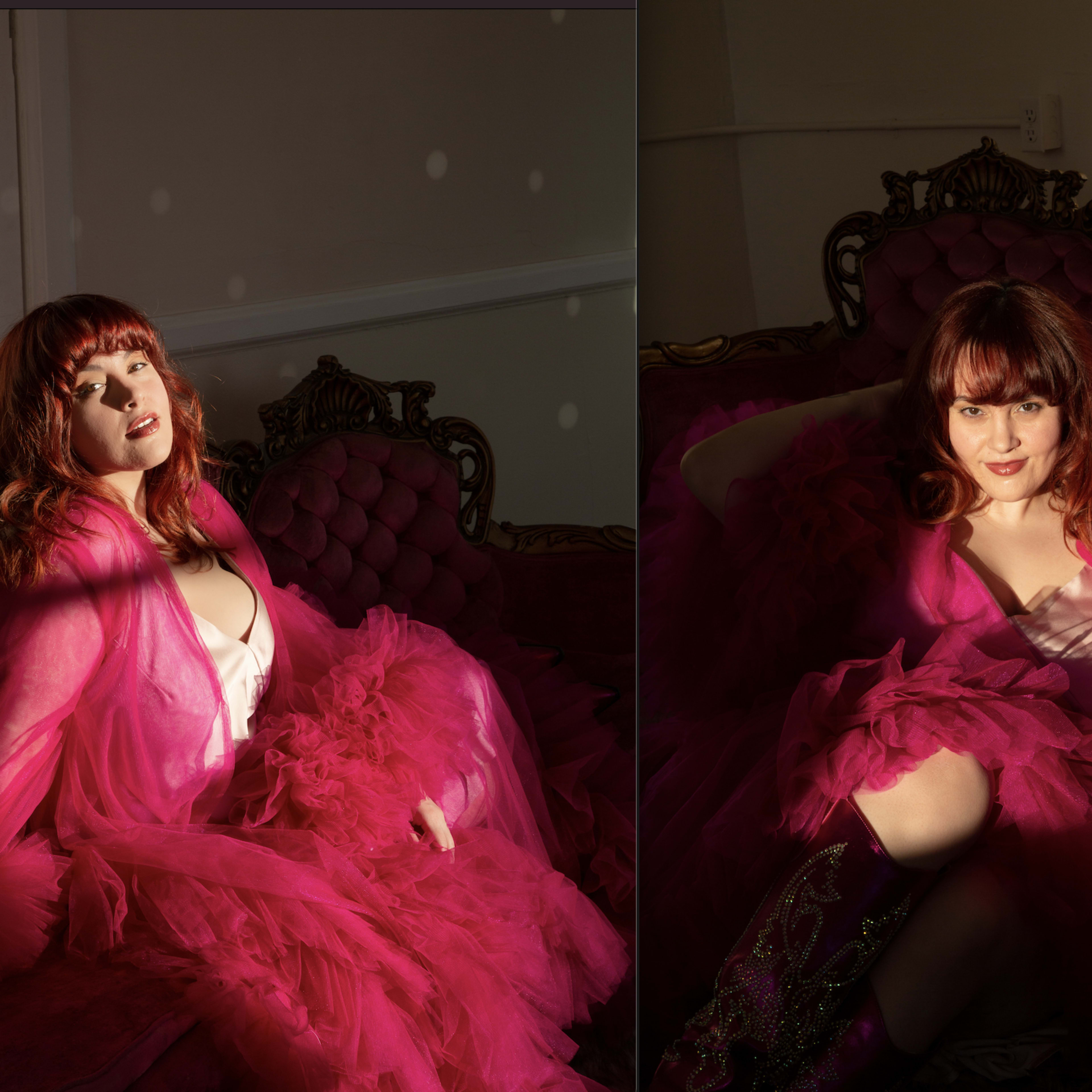 A woman in a pink feathered gown lounges on a vintage pink sofa in a well-lit room.