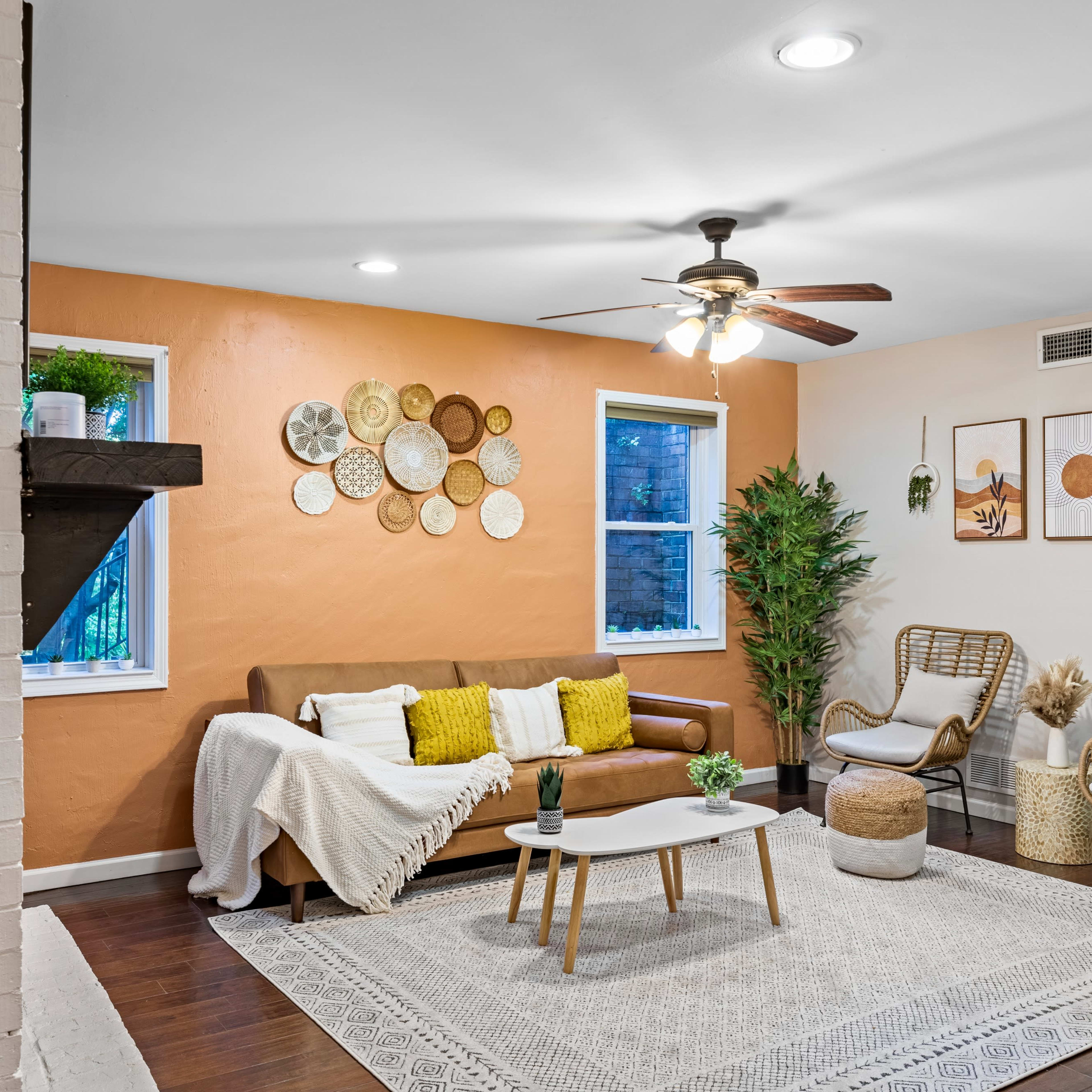 A living room with a brown sofa, a coffee table, two wicker chairs, and decorative wall art against an orange accent wall.
