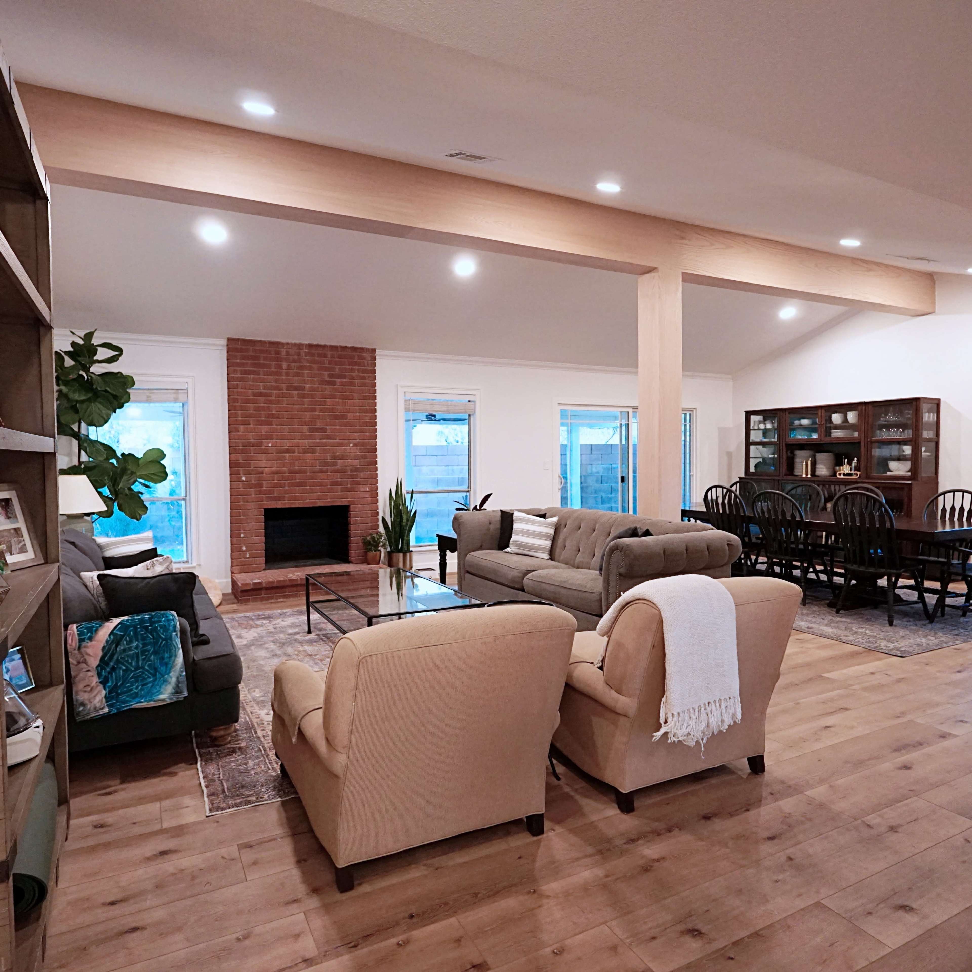 A spacious living area with a seating arrangement, a dining table, a brick fireplace, and large windows letting in natural light.