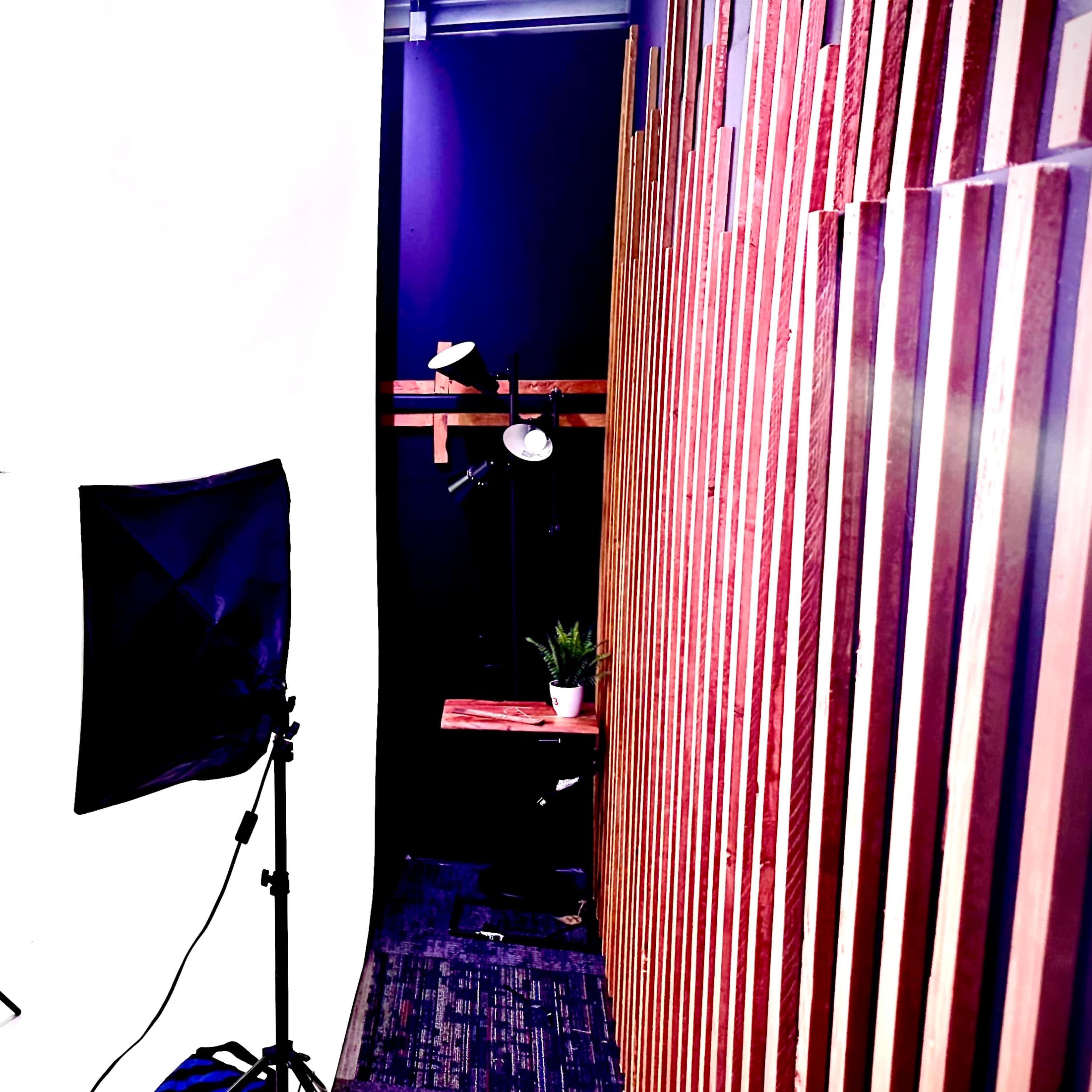 A photography studio setup with a white backdrop, two lighting stands, a reflector, and wooden paneling on one side.