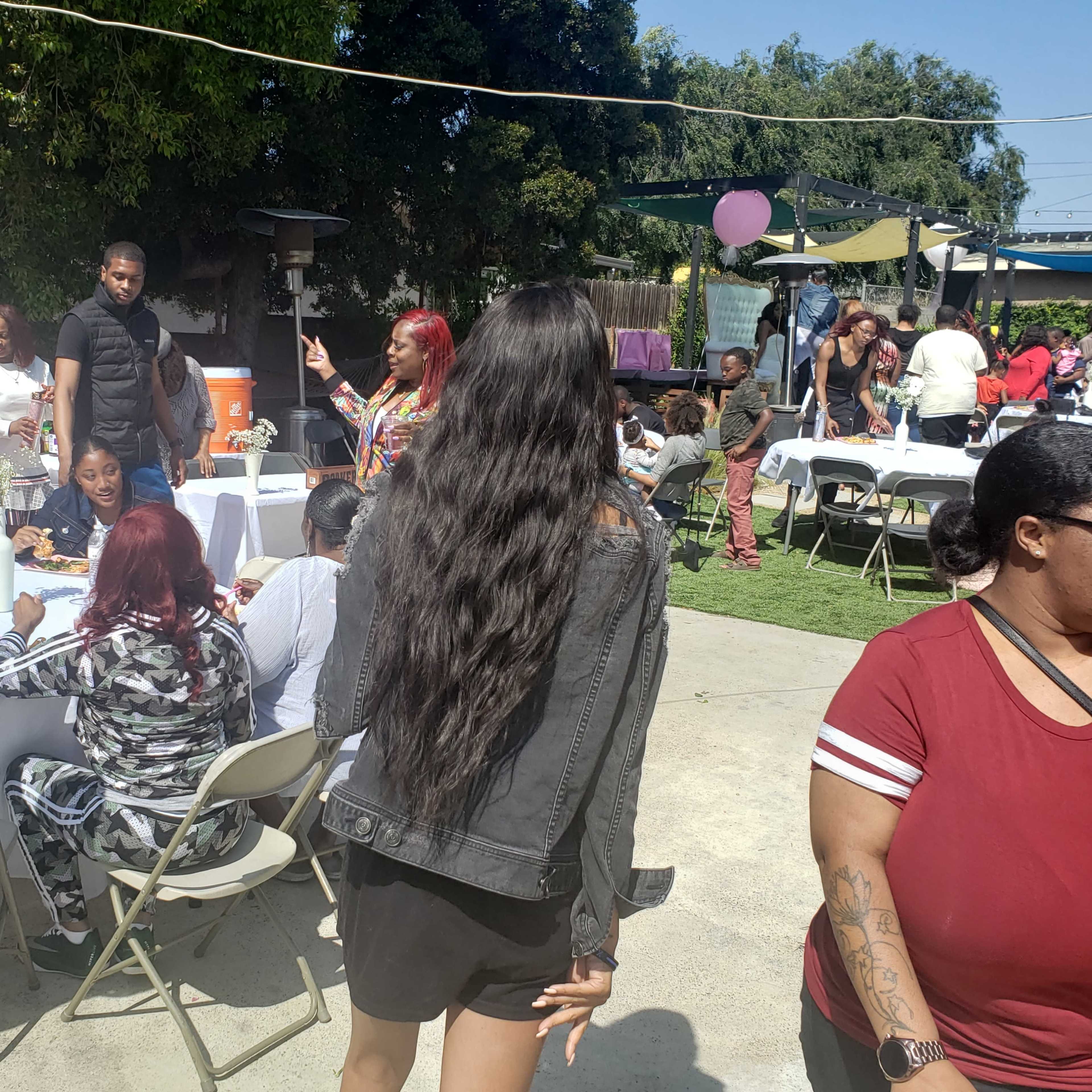 A group of people gather around tables at an outdoor event, enjoying food and socializing under a sunny sky.