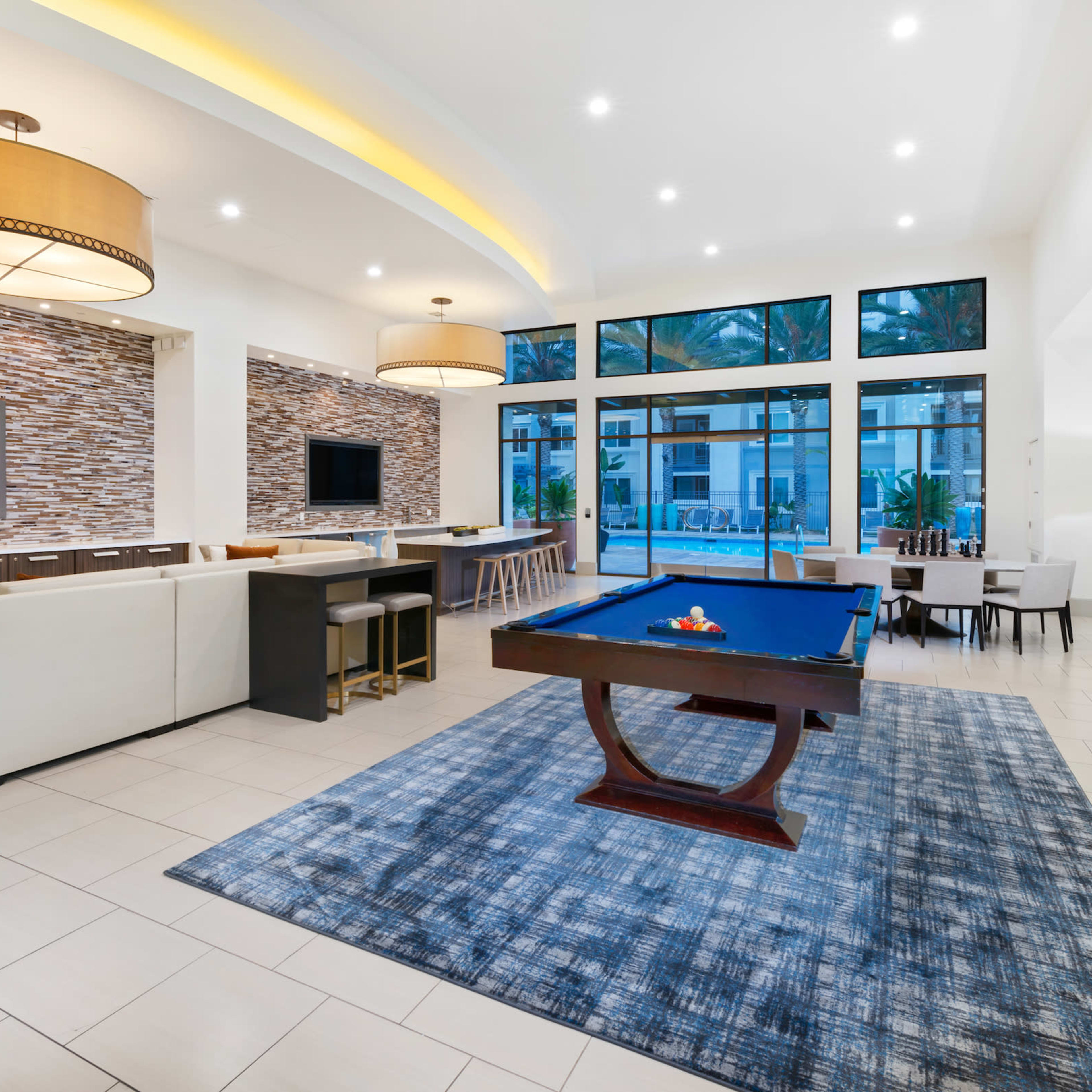 A modern communal lounge area featuring a pool table, multiple seating options, and large windows with natural light.