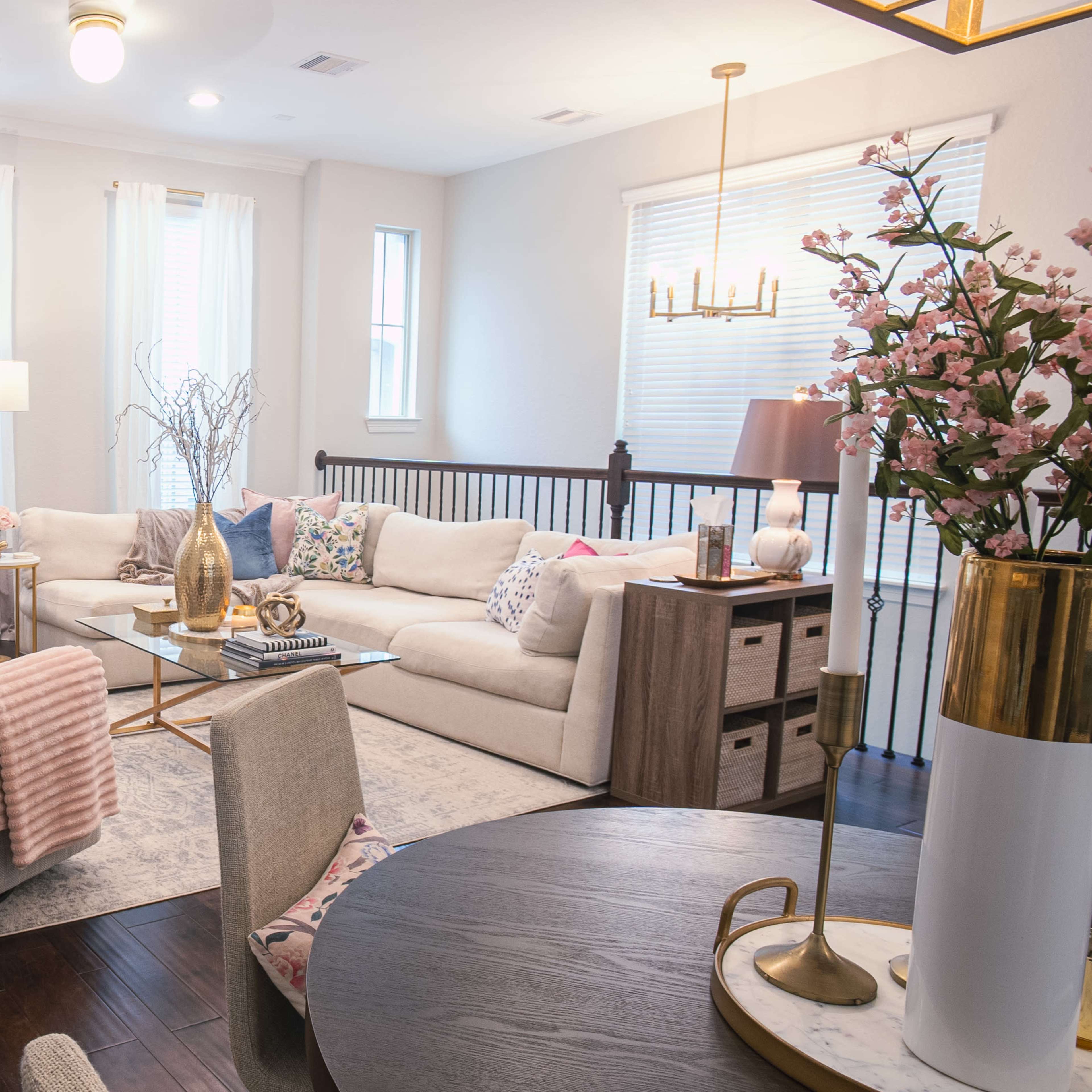 A light-filled living room features a beige sectional sofa, a glass coffee table, and decorative accents on a dark wood floor.