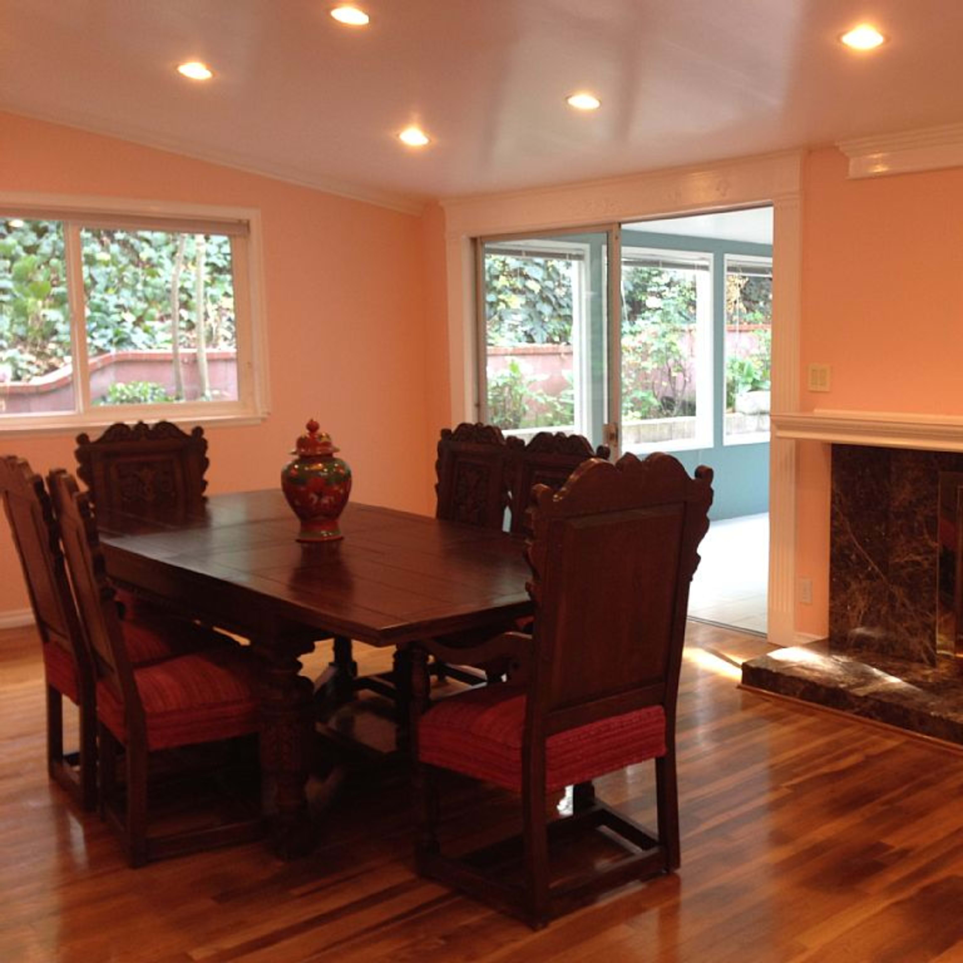 A dining area with a large wooden table and chairs, a decorative vase in the center, and a fireplace against a peach-colored wall.