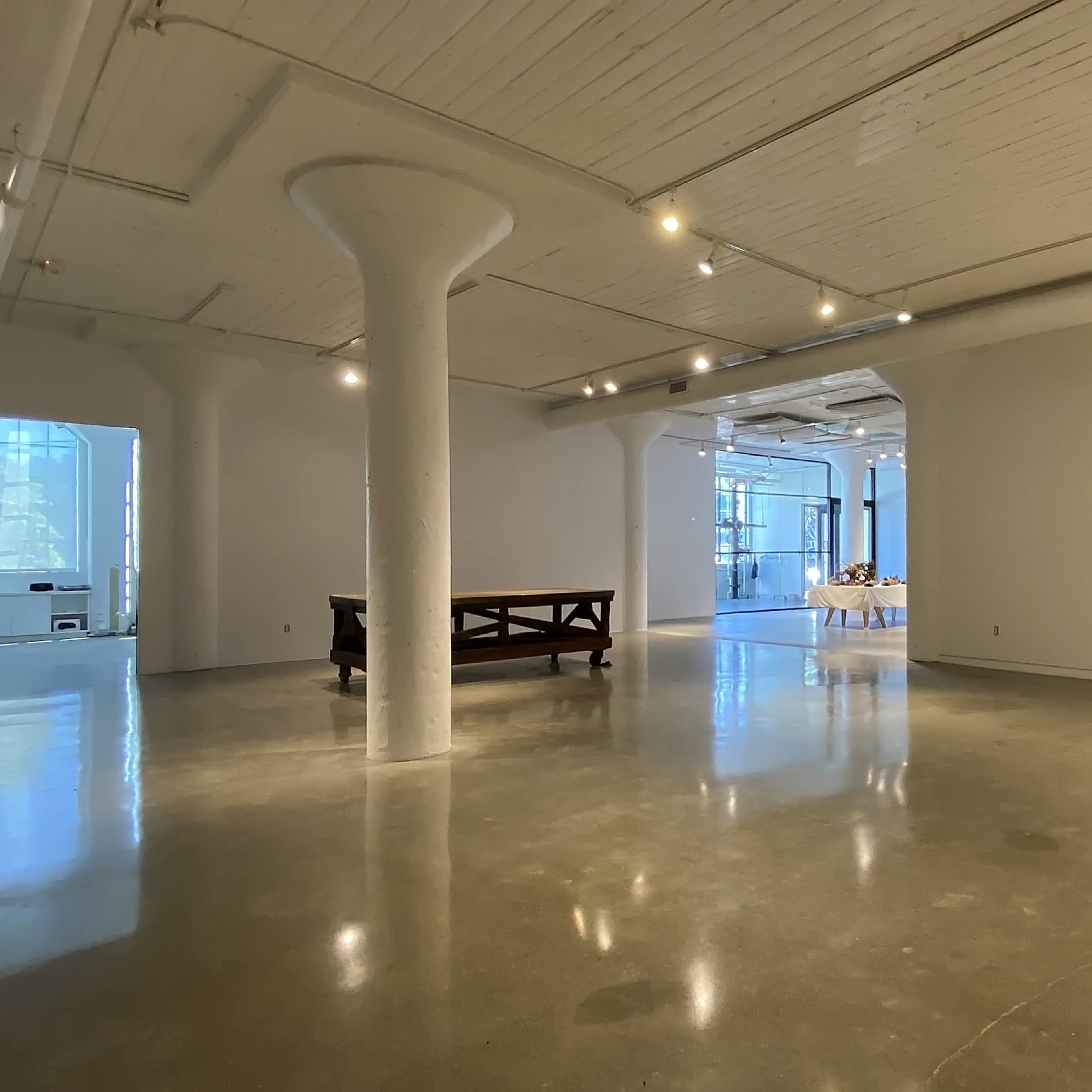 A spacious, minimally decorated art gallery with polished concrete floors and large windows allowing natural light.