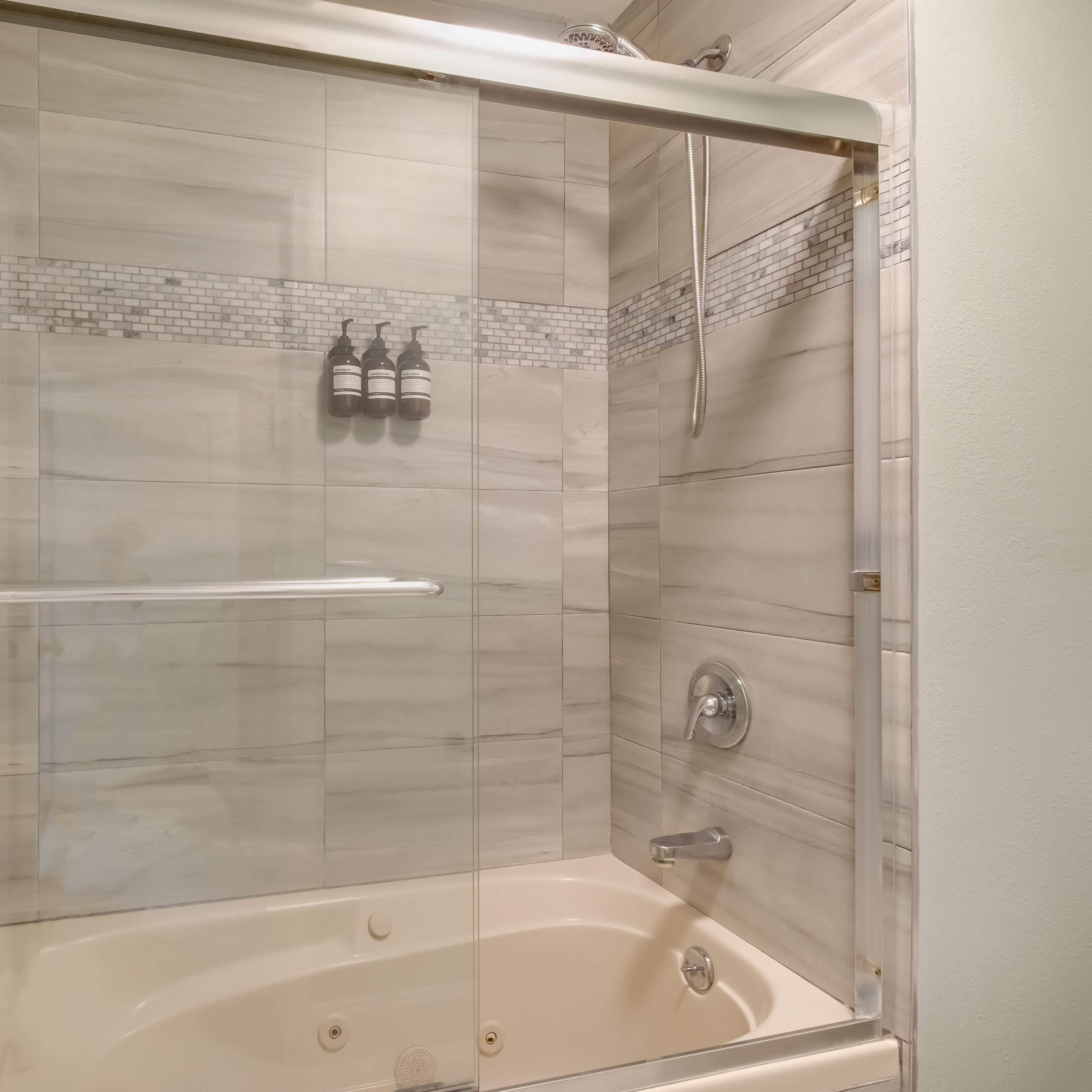 A bathroom with a glass shower enclosure, tiled walls, and a bathtub with a built-in showerhead.