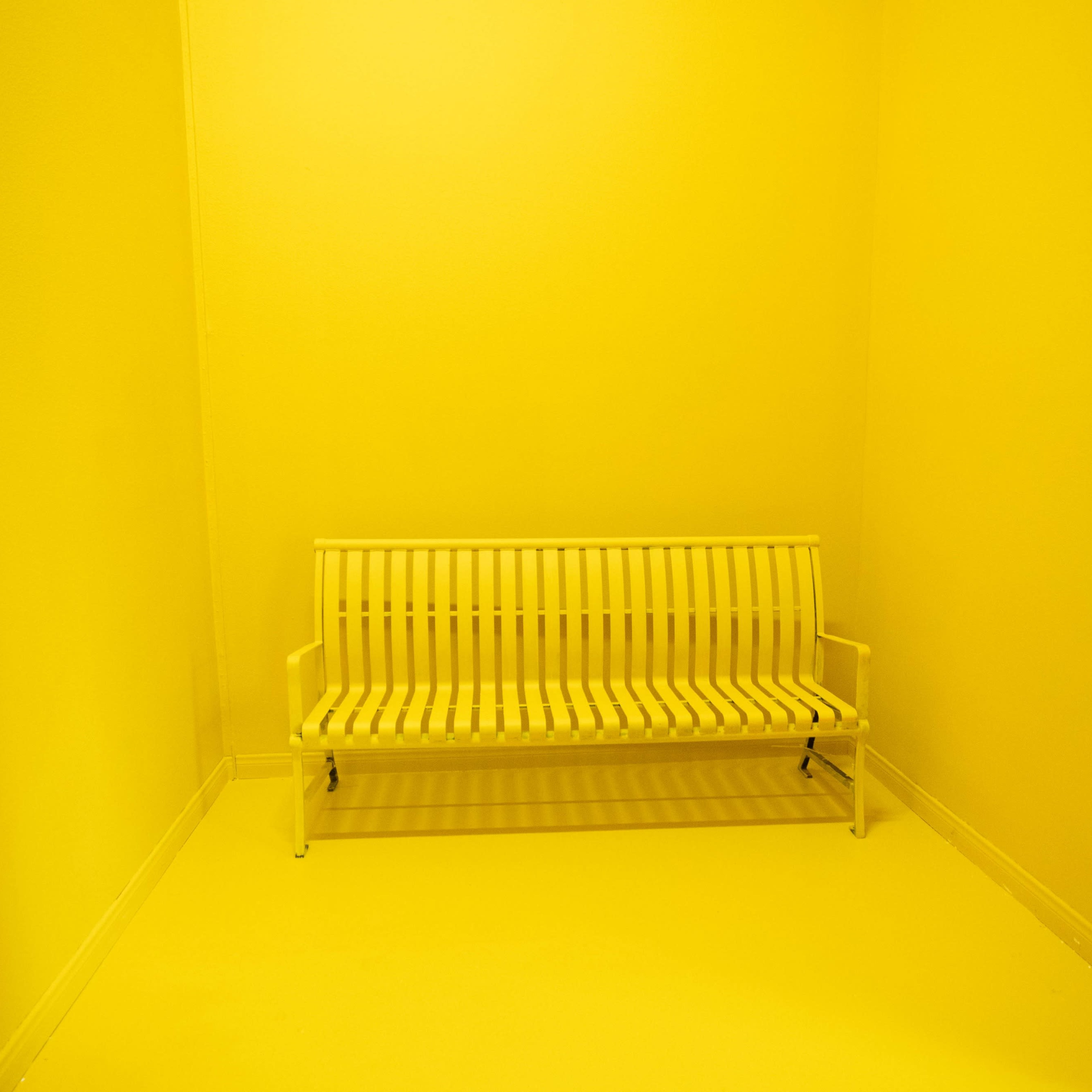 A white bench is positioned in a completely yellow room.